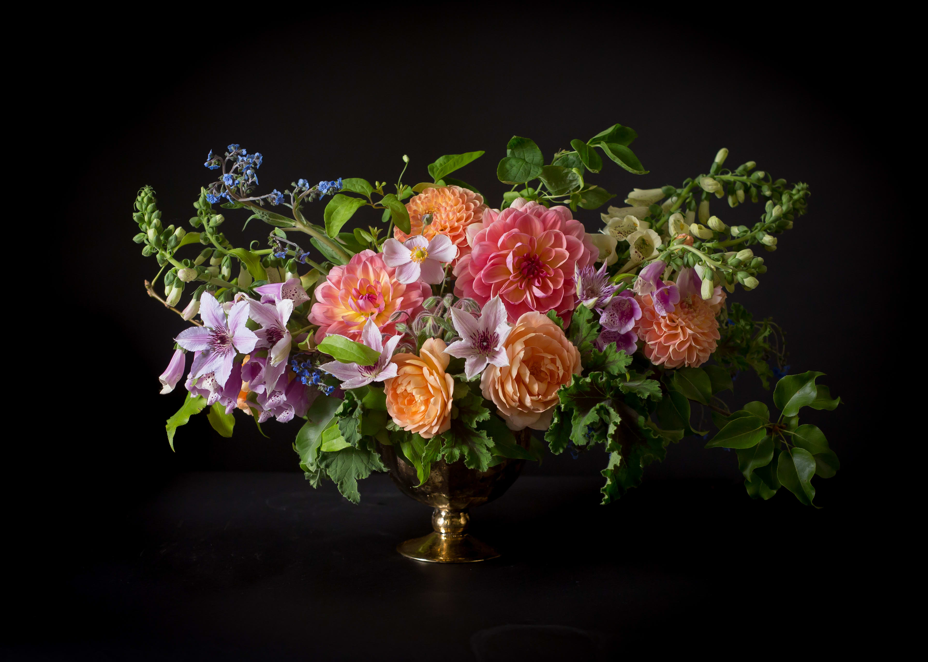Mixed bouquet of pink, peach, and lavender flowers in a gold vase