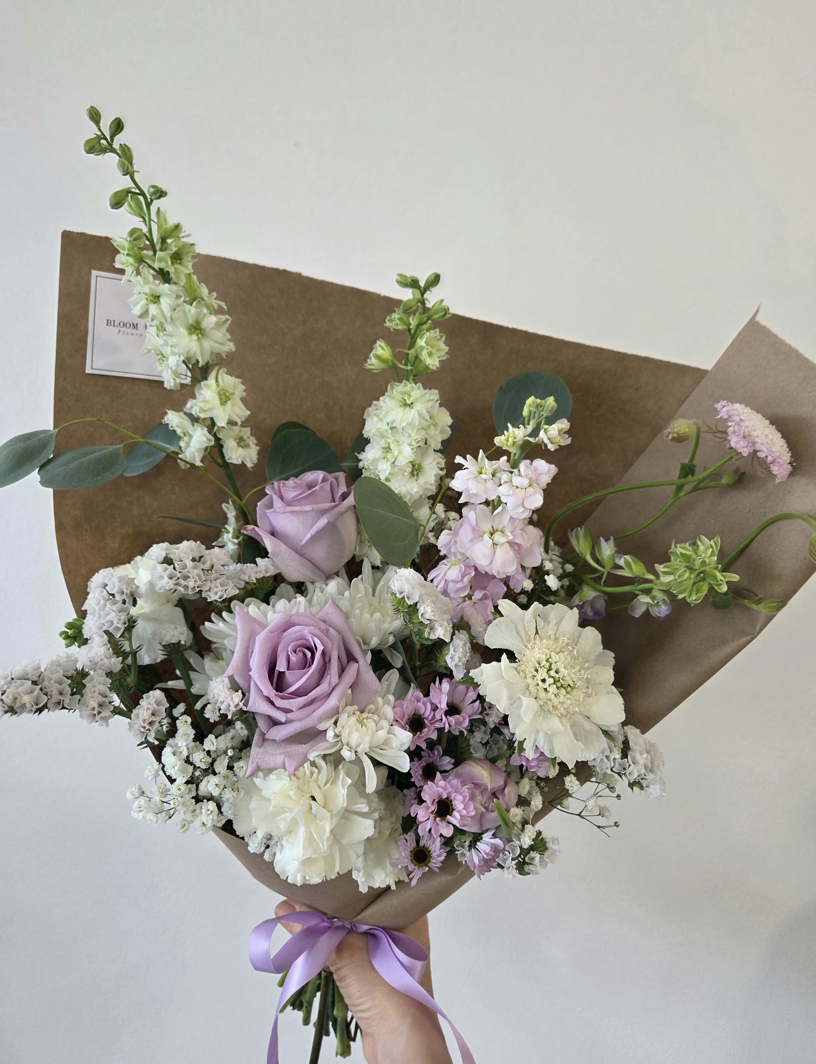 Hand-tied bouquet of lavender roses and white flowers wrapped in brown paper
