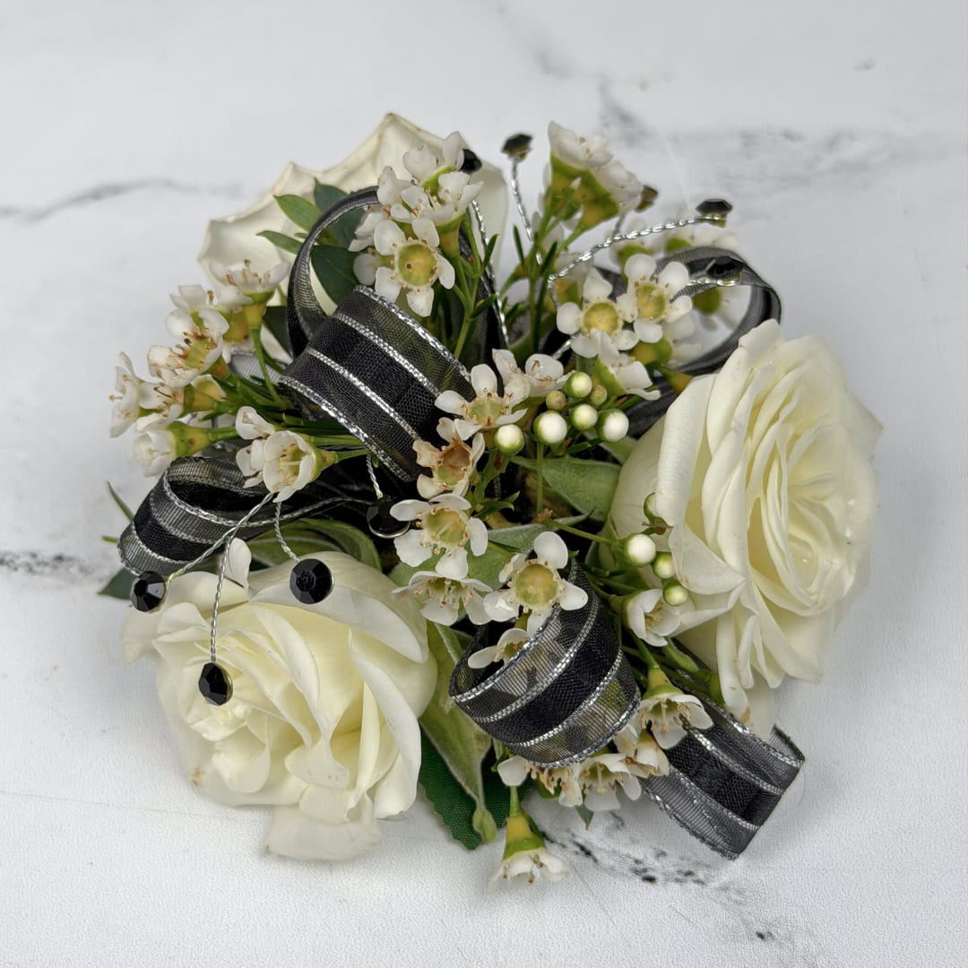 Onyx 3 Rose Wrist Corsage - Cream-white roses contrasted with black and silver shimmering ribbon make this wrist corsage a quietly dramatic pick for prom or any formal evening event. The Onyx 3 Rose Corsage blends the classic romance of roses with modern contrast so the person you're celebrating looks polished and unforgettable on the dance floor.  Three cream-white roses are nestled among tiny white filler blossoms for soft texture and a fresh, natural look. Black and silver ribbon loops and decorative gem-like rhinestones create an artful, tailored finish, all held together on a white lace wristlet for easy wearing. The restrained color scheme reads elegant and adaptable, perfect for an outfit that deserves some striking contrast.
