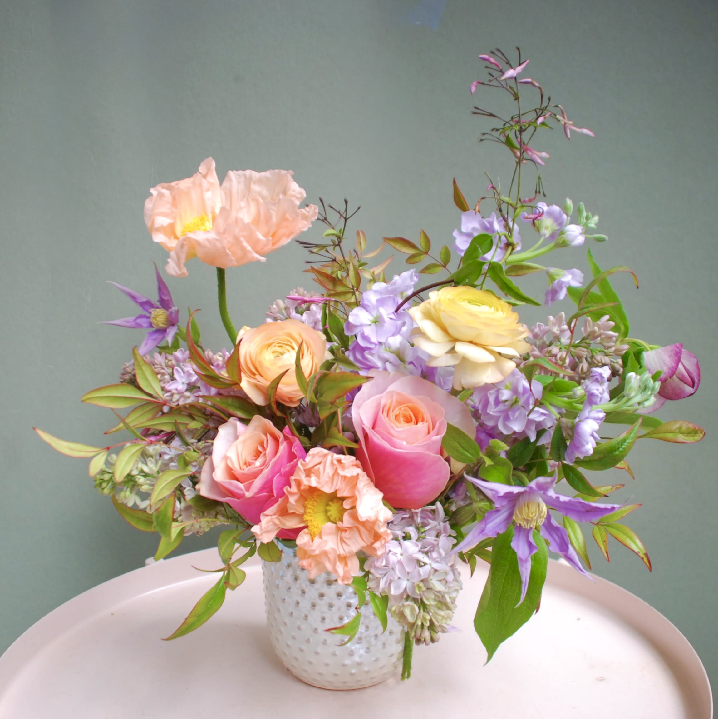 My heart - Soft pink and peach roses mingle with pale lavender stock and airy Icelandic poppies in a loose, garden-style bouquet-an ideal flower arrangement for Mother's Day, birthdays, anniversaries, or a tender "thinking of you" moment. The pastel palette and natural, asymmetrical silhouette give the recipient a light, whimsical impression that reads romantic enough for love and anniversaries yet gentle for get well, sympathy, or simply saying thank you.  Arranged in a white textured ceramic vase, stems and soft greenery spill outward to create movement and a fresh-picked feel. The mix of roses, poppies, stock, and complementary blooms offers varied textures-velvety petals, feathery poppy centers, and delicate sprays of filler-for a full but airy composition that suits spring and summer gifting alike.  Perfect for the person you want to make feel seen-whether you're celebrating a retirement, offering congratulations, apologizing, or brightening a "just because" day-this arrangement arrives ready to display. Standard care: keep fresh water in the vase, trim stems slightly when refreshing water, and place away from direct heat or drafts to prolong bloom life.