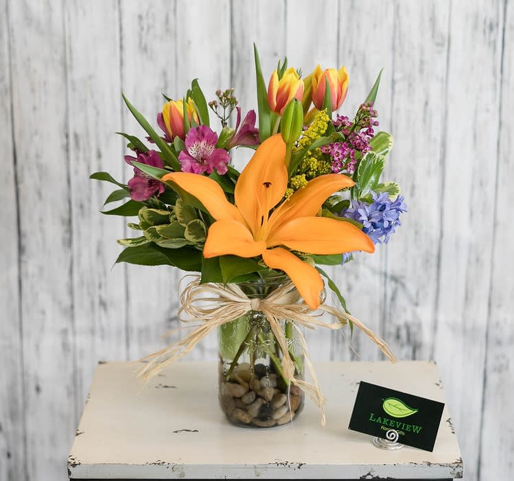 Mixed bouquet with orange lily and colorful tulips in a glass vase
