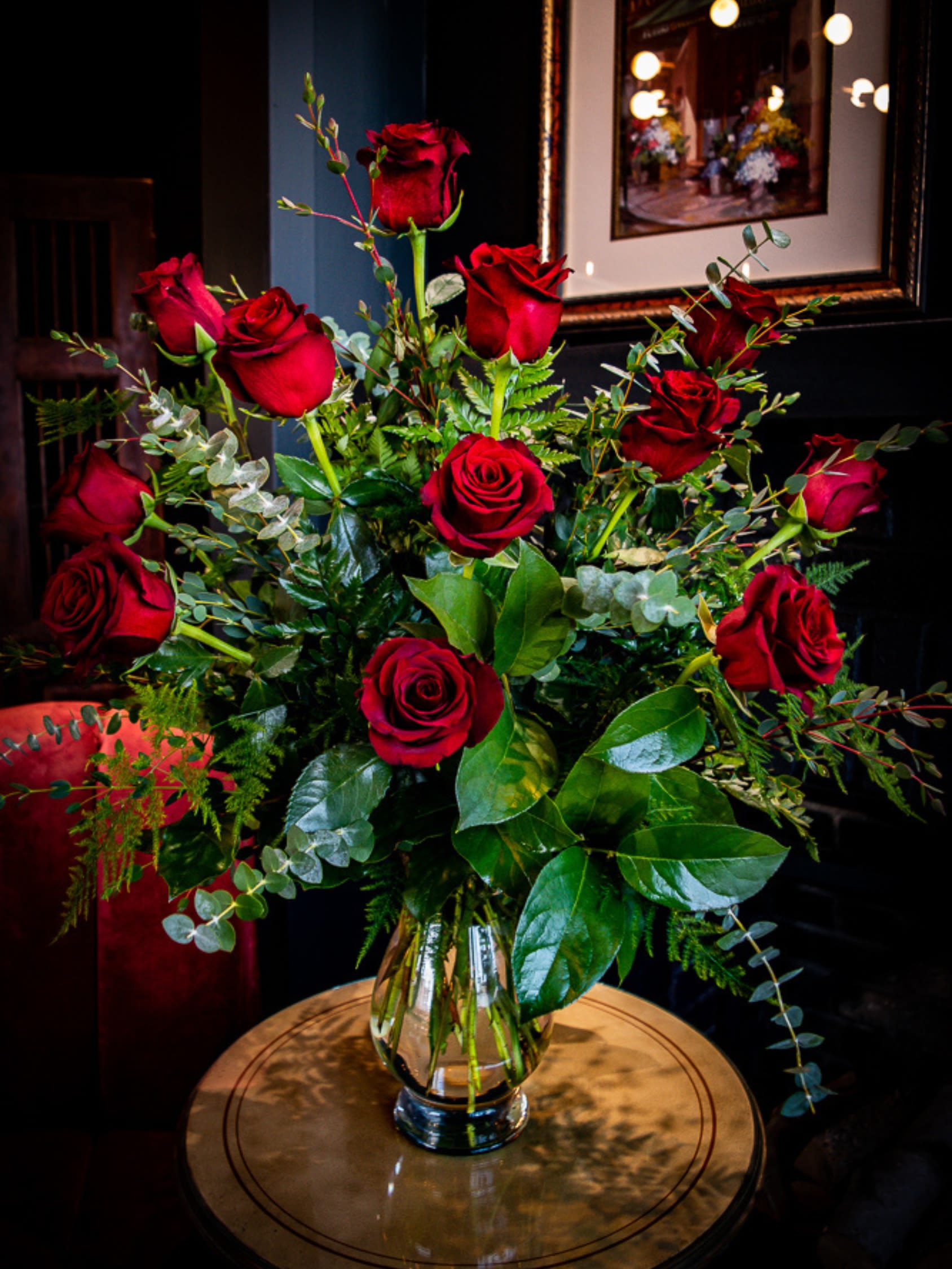 Red roses arranged in a clear glass vase with mixed greenery