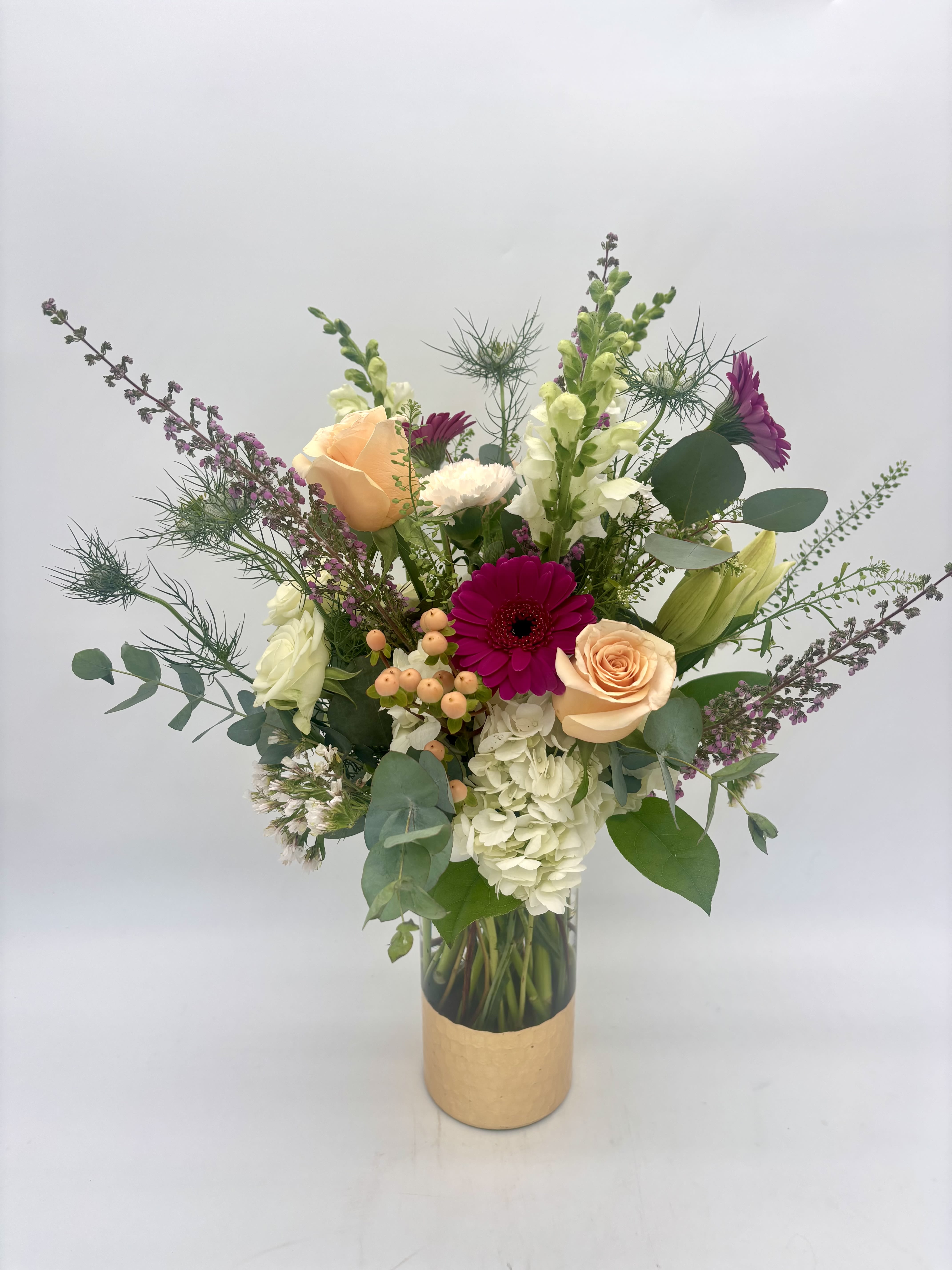 Tall mixed arrangement with peach roses, fuchsia gerbera daisies, white hydrangeas and snapdragons in a glass vase