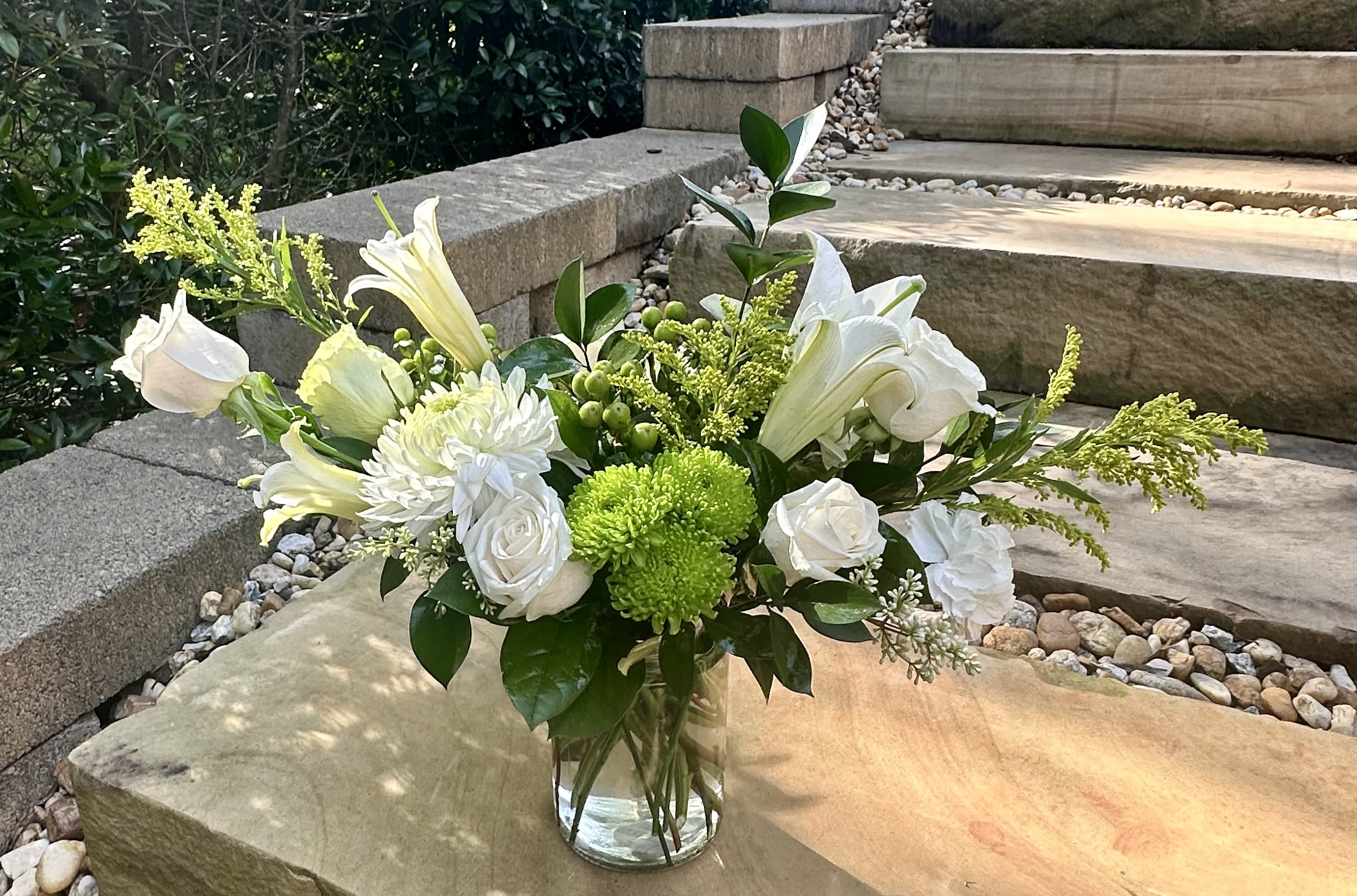 White flowers and green blooms arranged in a clear glass vase