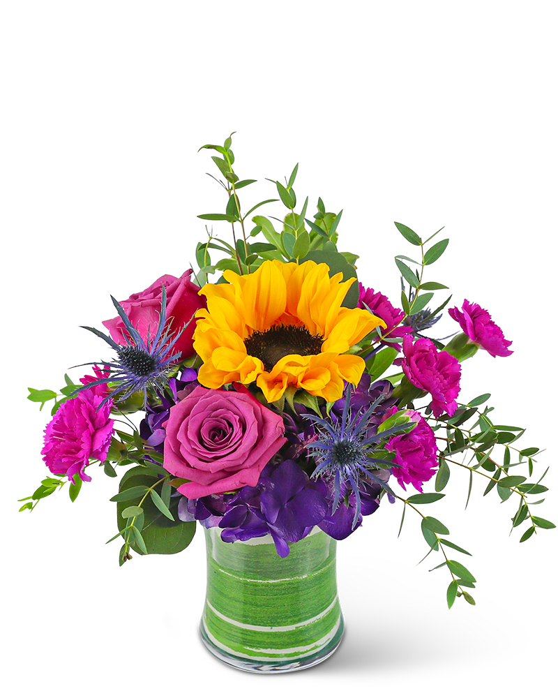 Mixed bouquet with yellow sunflower, purple rose, hot pink carnations, and blue thistle in a glass vase