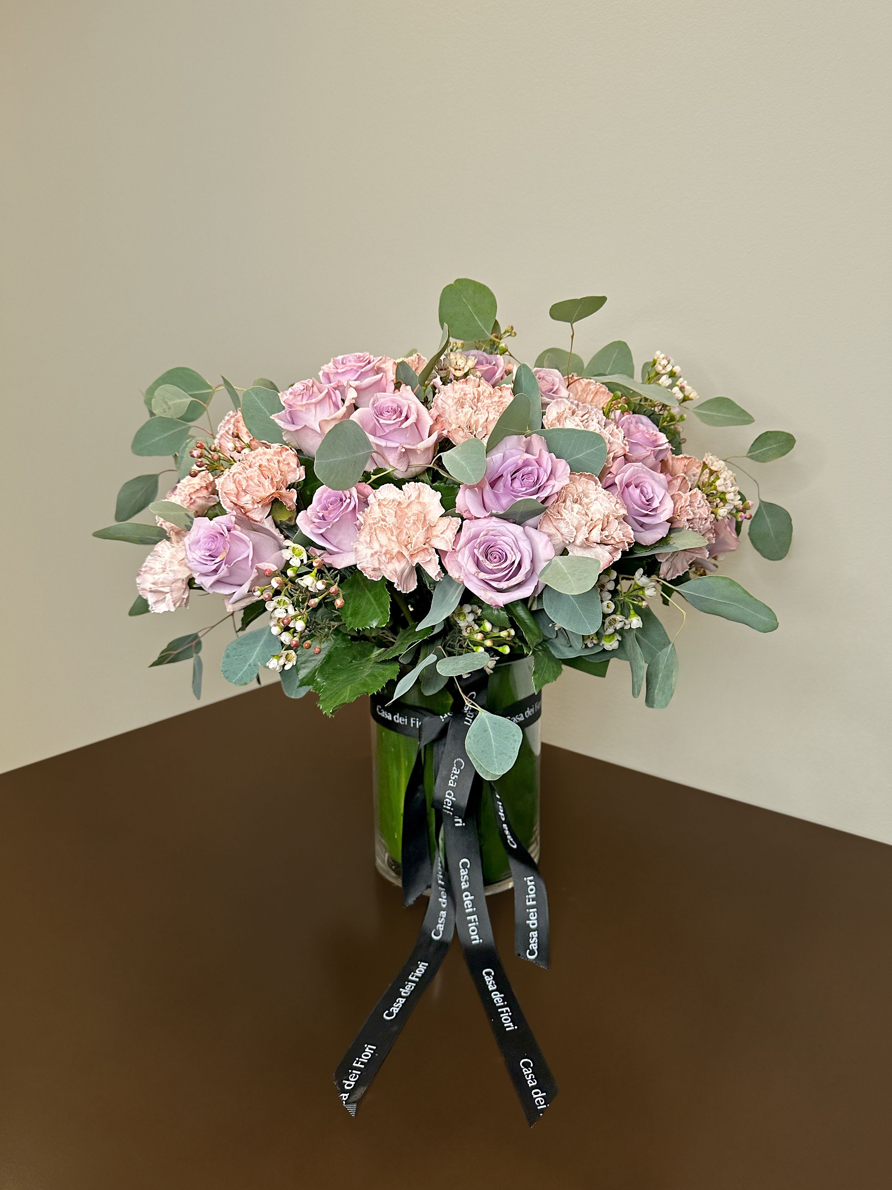 Pink roses and carnations arranged in a glass vase with a ribbon