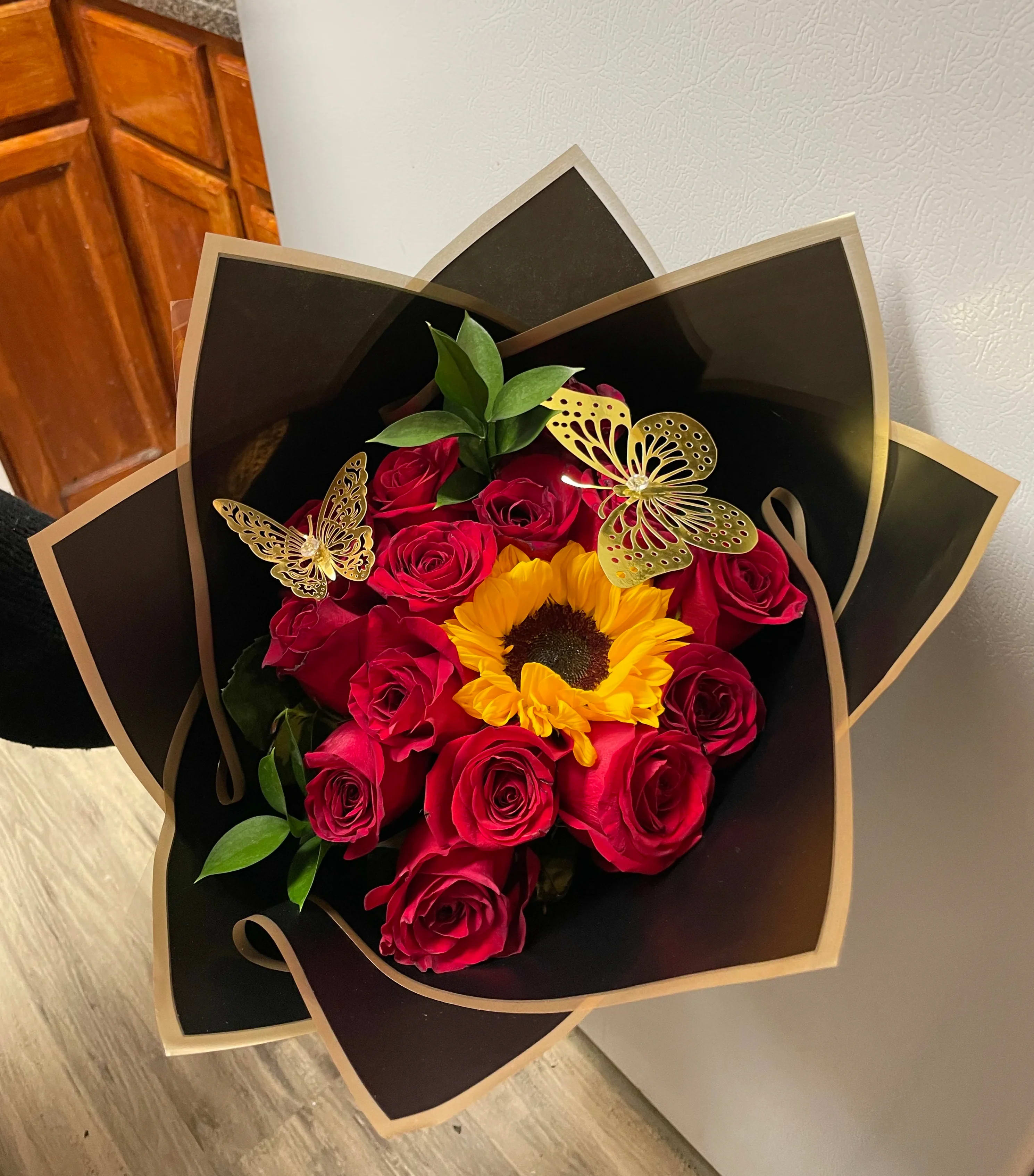Bouquet of red roses and a sunflower in black wrapping with gold butterfly accents