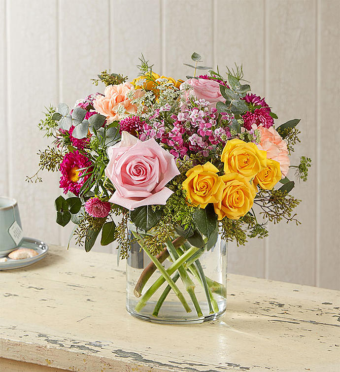 Mixed bouquet of pink, yellow, and peach flowers in a clear glass vase