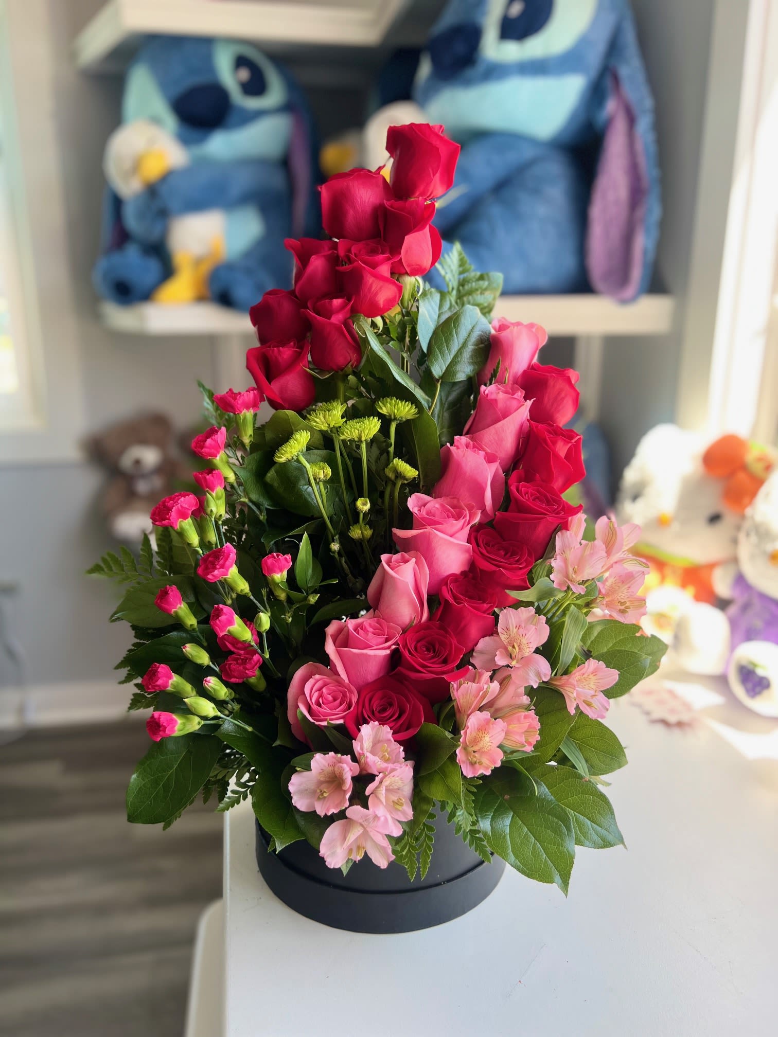 Sandy - Compact black round box filled with red and pink roses, pink spray carnations and green filler-full, layered look