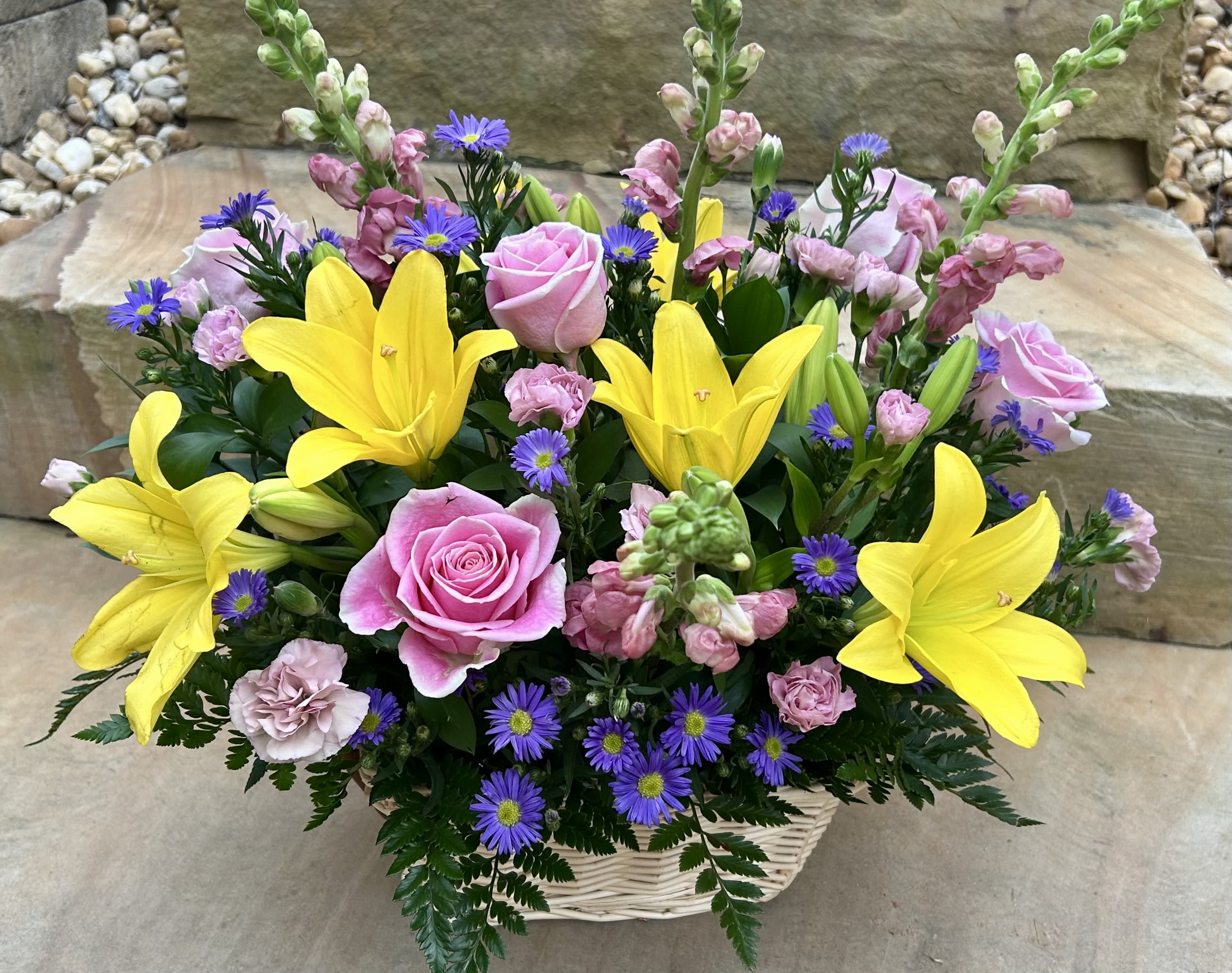 Basket arrangement with pink roses, yellow lilies, and purple daisies