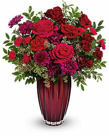 Red and pink roses with purple mums in a tall burgundy vase