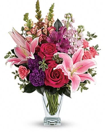Mixed bouquet of pink lilies, roses, and purple flowers in a clear glass vase