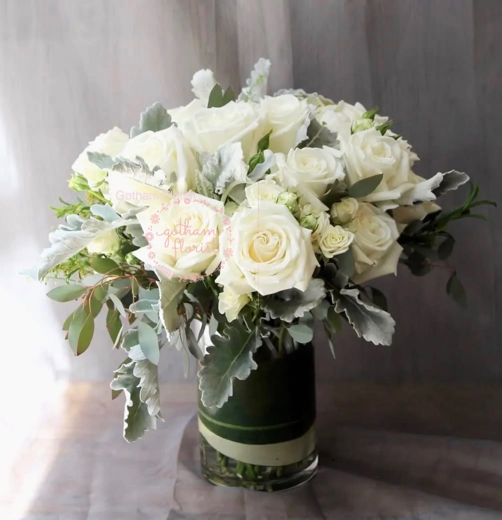 White roses arranged in a glass vase with silvery foliage