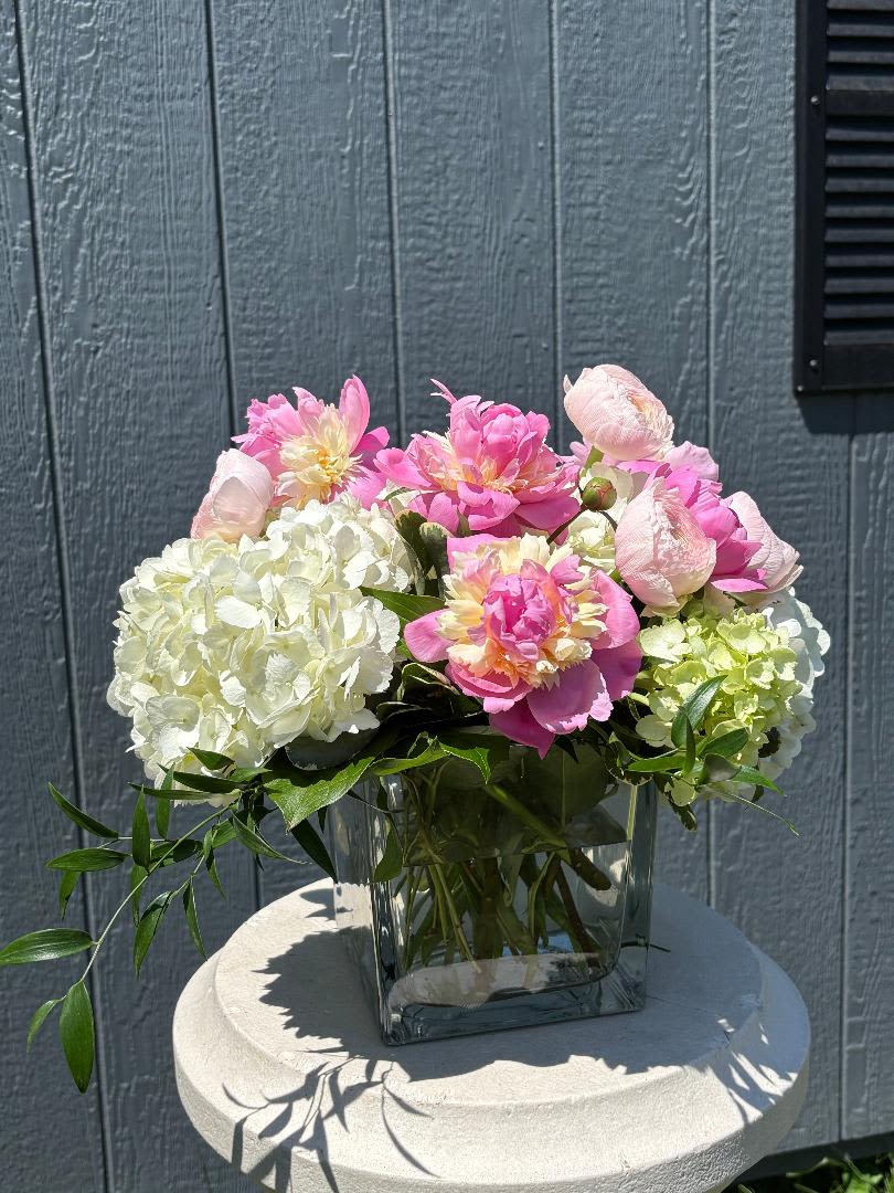 Pretty in Peony - Meet Pretty in Peony—a soft, romantic arrangement designed to make a statement. Featuring lush peonies, delicate ranunculus, and full hydrangea, this design is all about dreamy texture and fresh-from-the-garden charm.  Perfect for celebrations, heartfelt gifts, or simply treating yourself, Pretty in Peony brings an effortless elegance to any space.  Available in three sizes, with our Standard design shown at $160. Each arrangement is thoughtfully styled using the freshest seasonal blooms, so colors may vary slightly while maintaining this signature look.