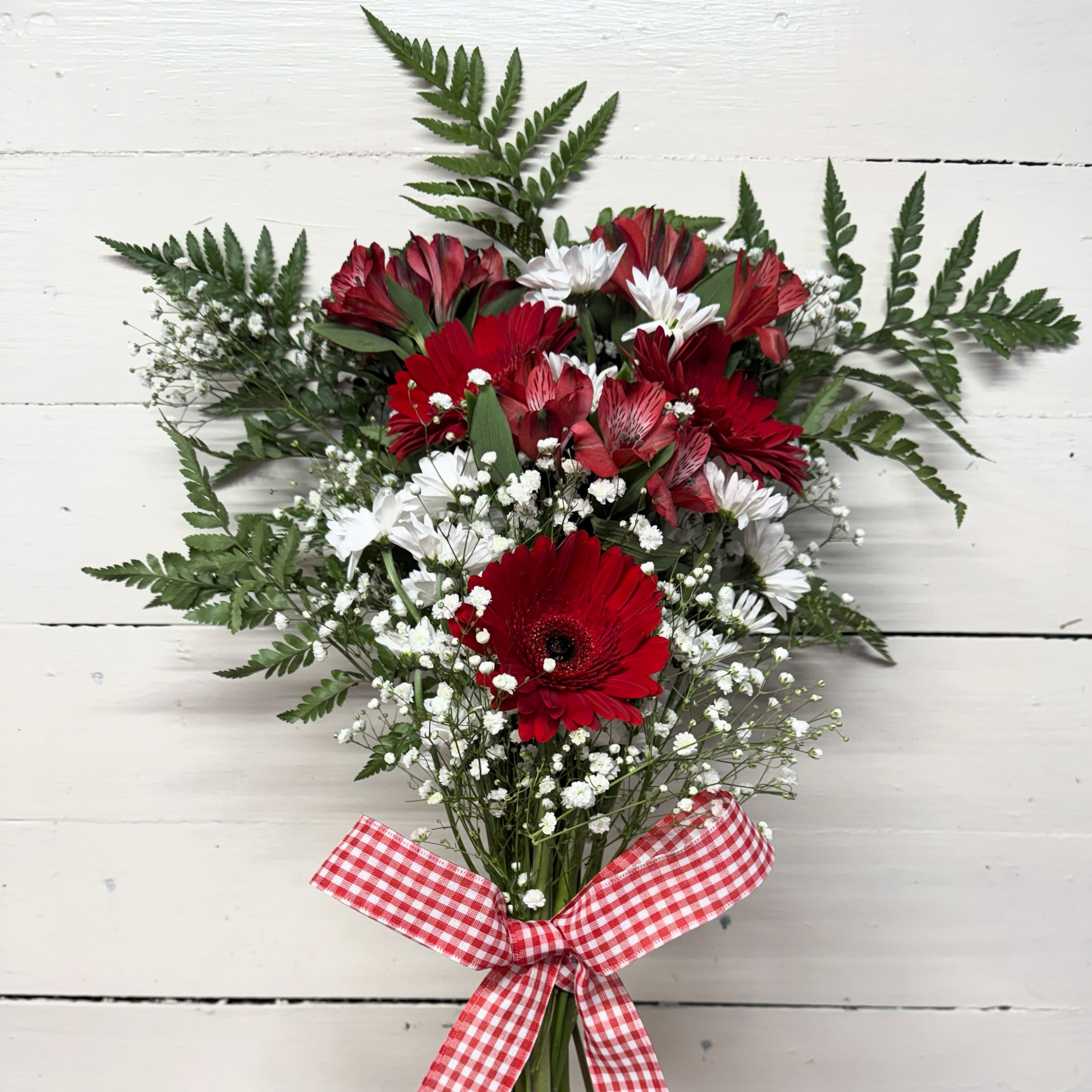Red and white bouquet with daisies and baby's breath tied with a gingham ribbon