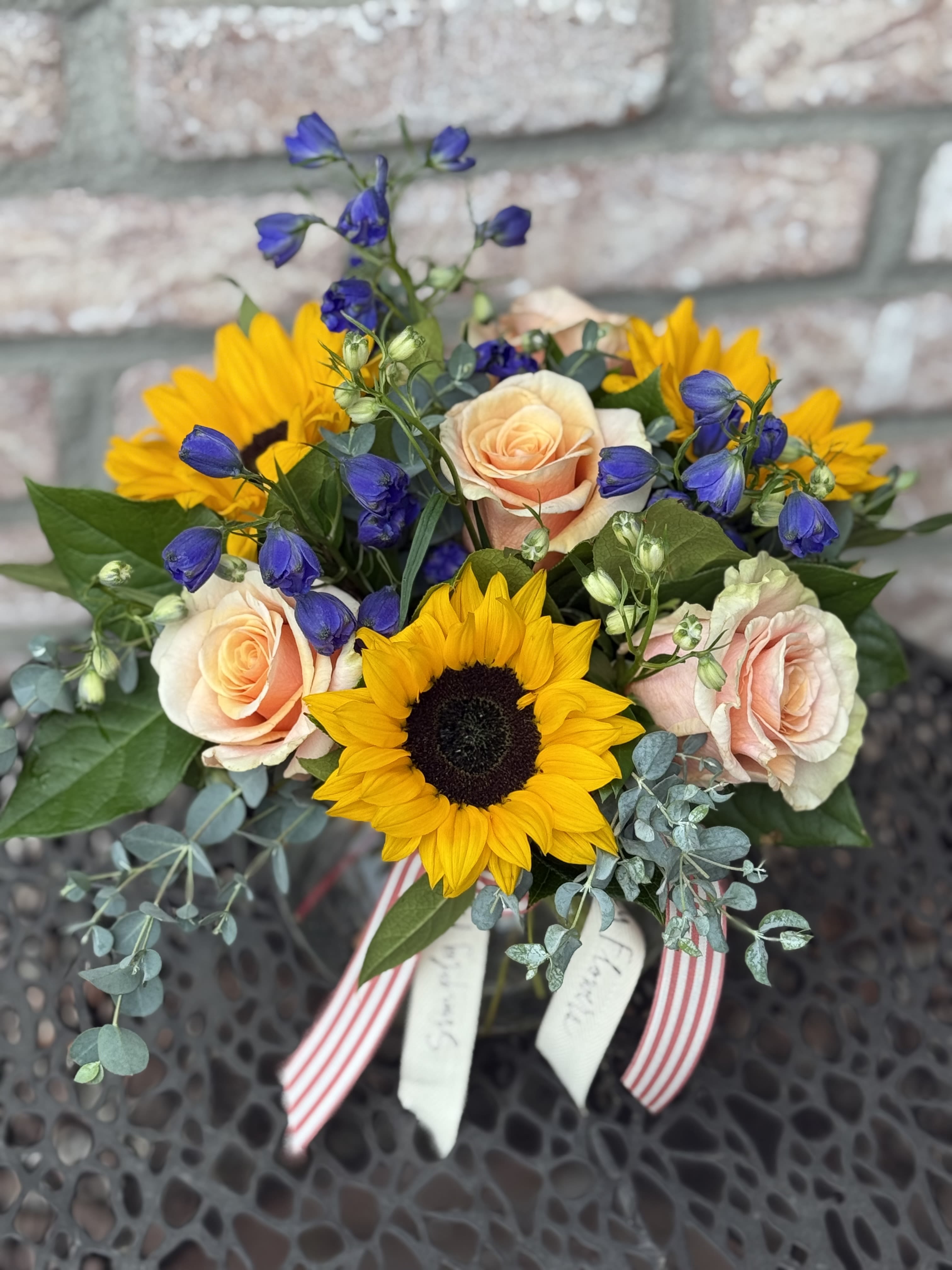 Bouquet of sunflowers, peach roses, and blue bellflowers with ribbon tails
