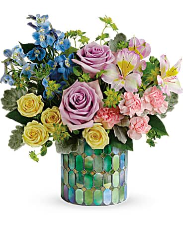 Mixed bouquet of roses, lilies, and blue flowers in a mosaic vase