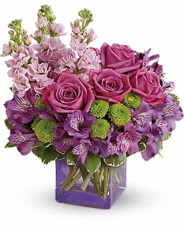 Purple roses and mixed purple flowers in a square glass vase
