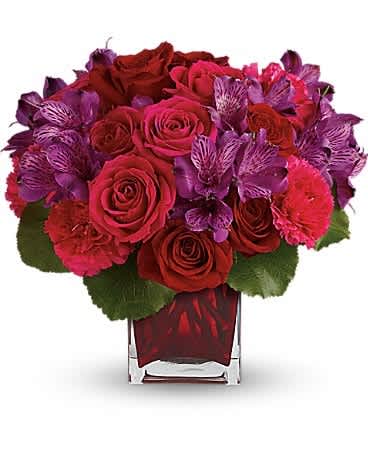 Red roses and purple flowers arranged in a clear square vase