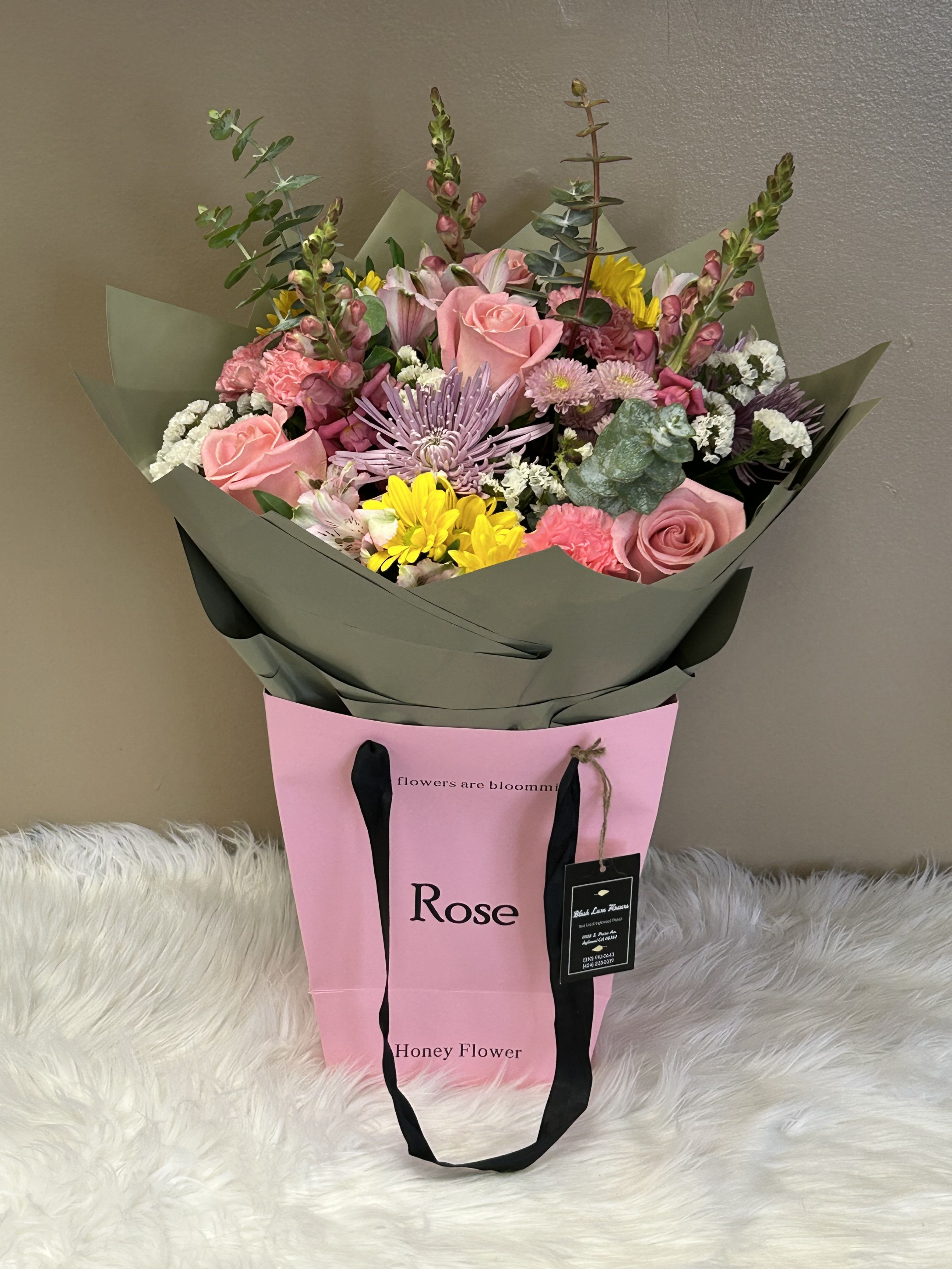 Mixed bouquet of pink roses, yellow blooms, and lavender flowers in a pink gift bag