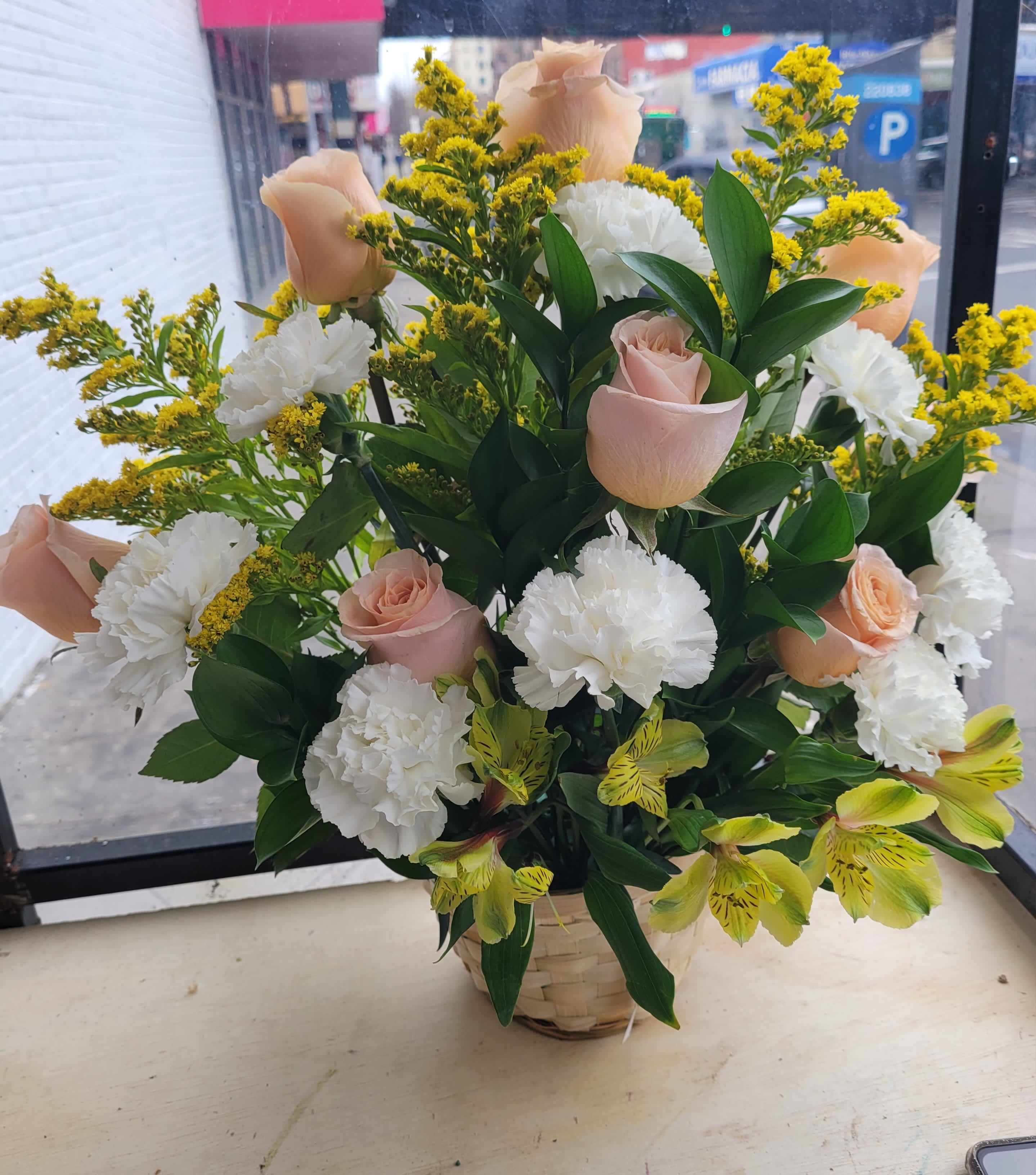 Basket arrangement of pale pink roses, white carnations, and yellow filler flowers