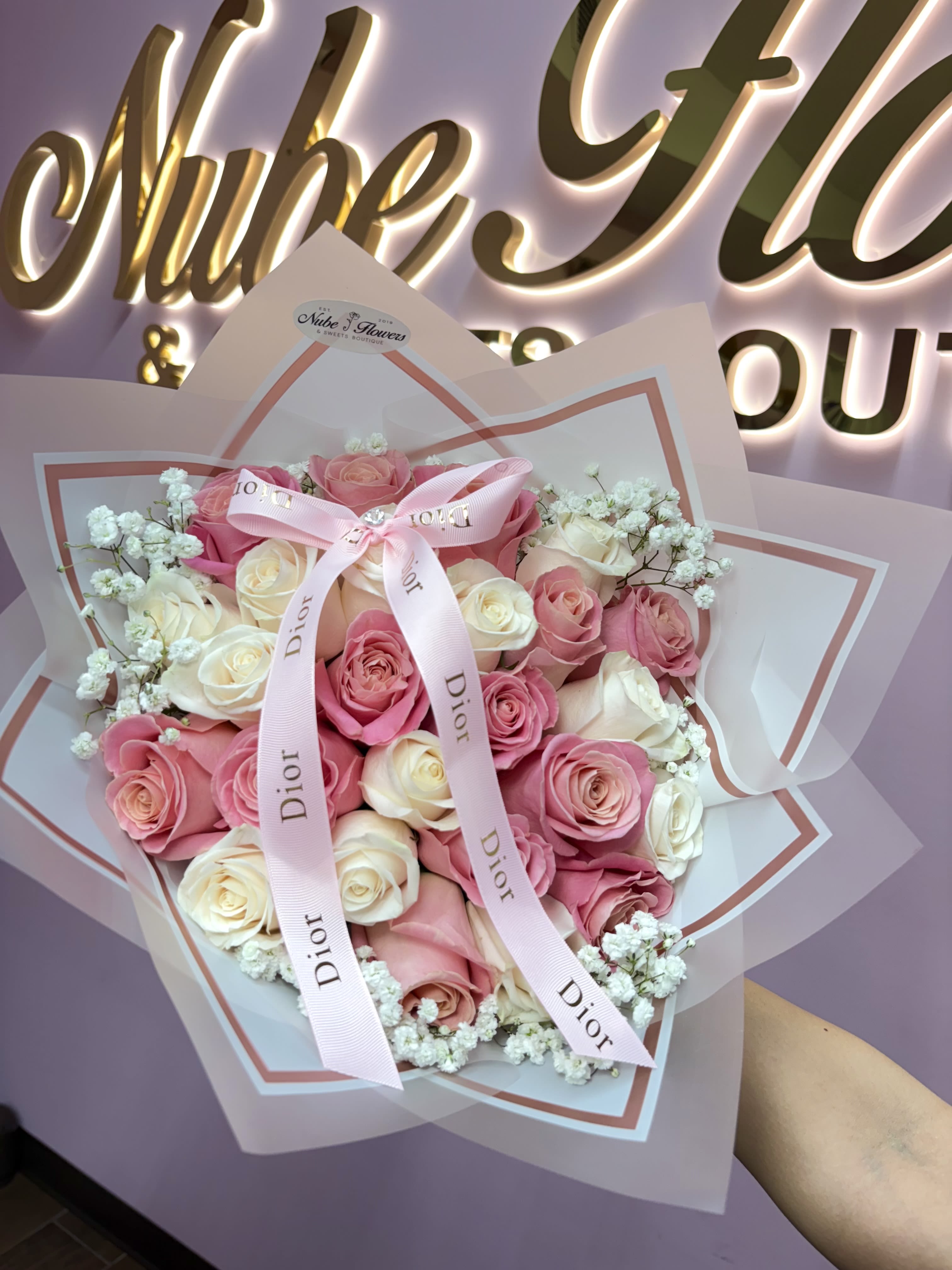 Dior Mom - Rounded hand-tied bouquet of pink and white roses with delicate fillers, layered pale wrap and pink ribbon