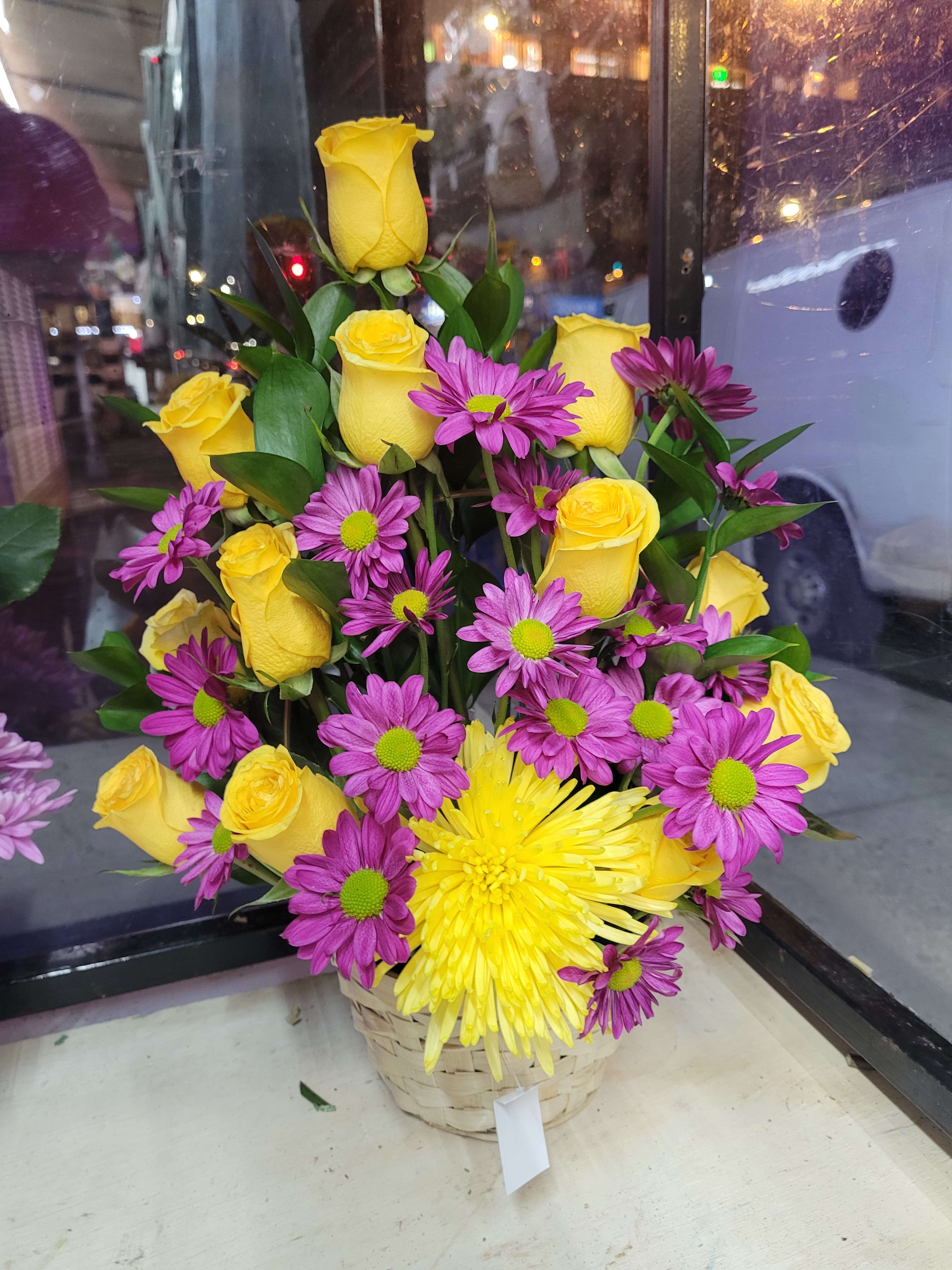 Basket arrangement of yellow roses and purple daisies