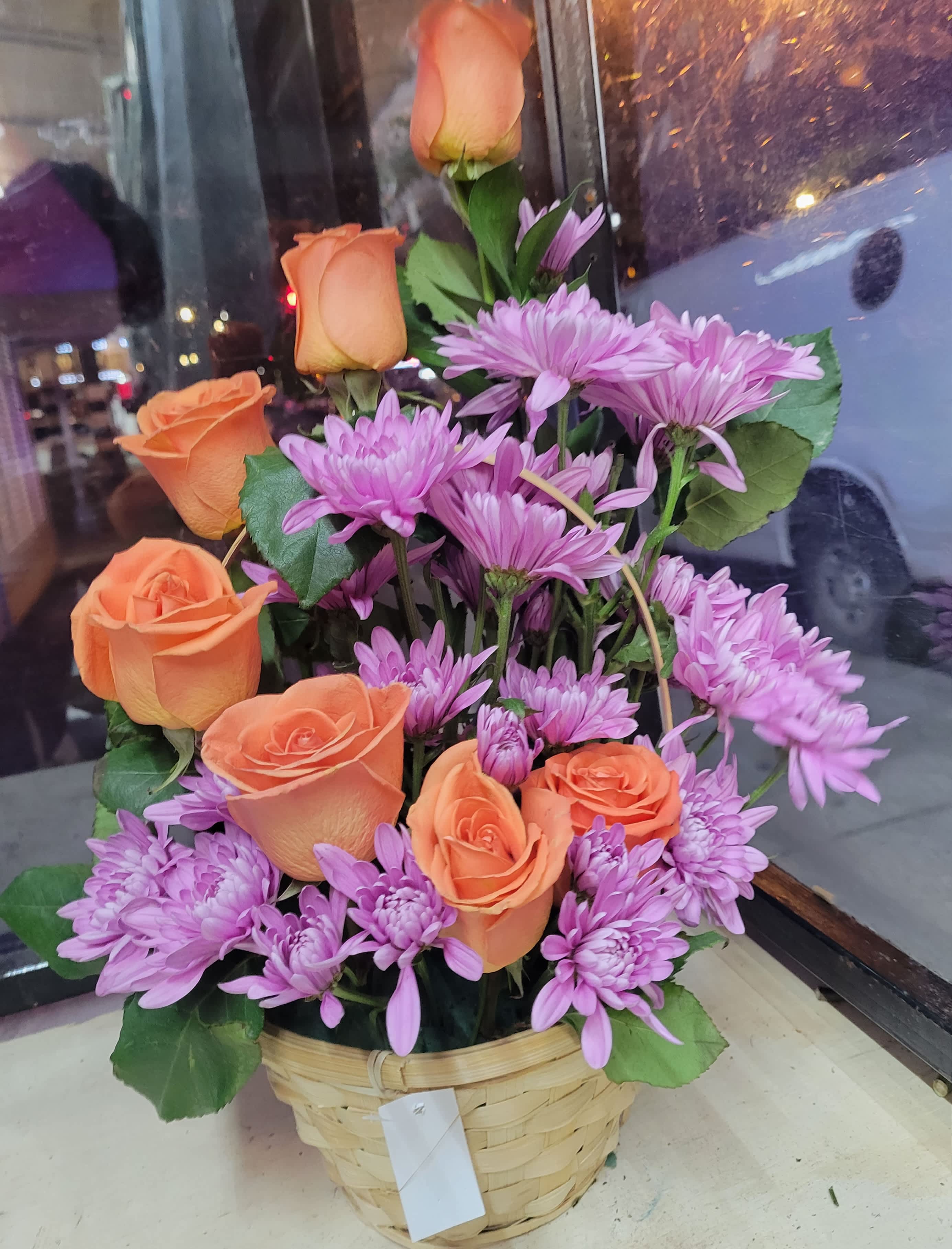 Basket arrangement of orange roses and purple daisies