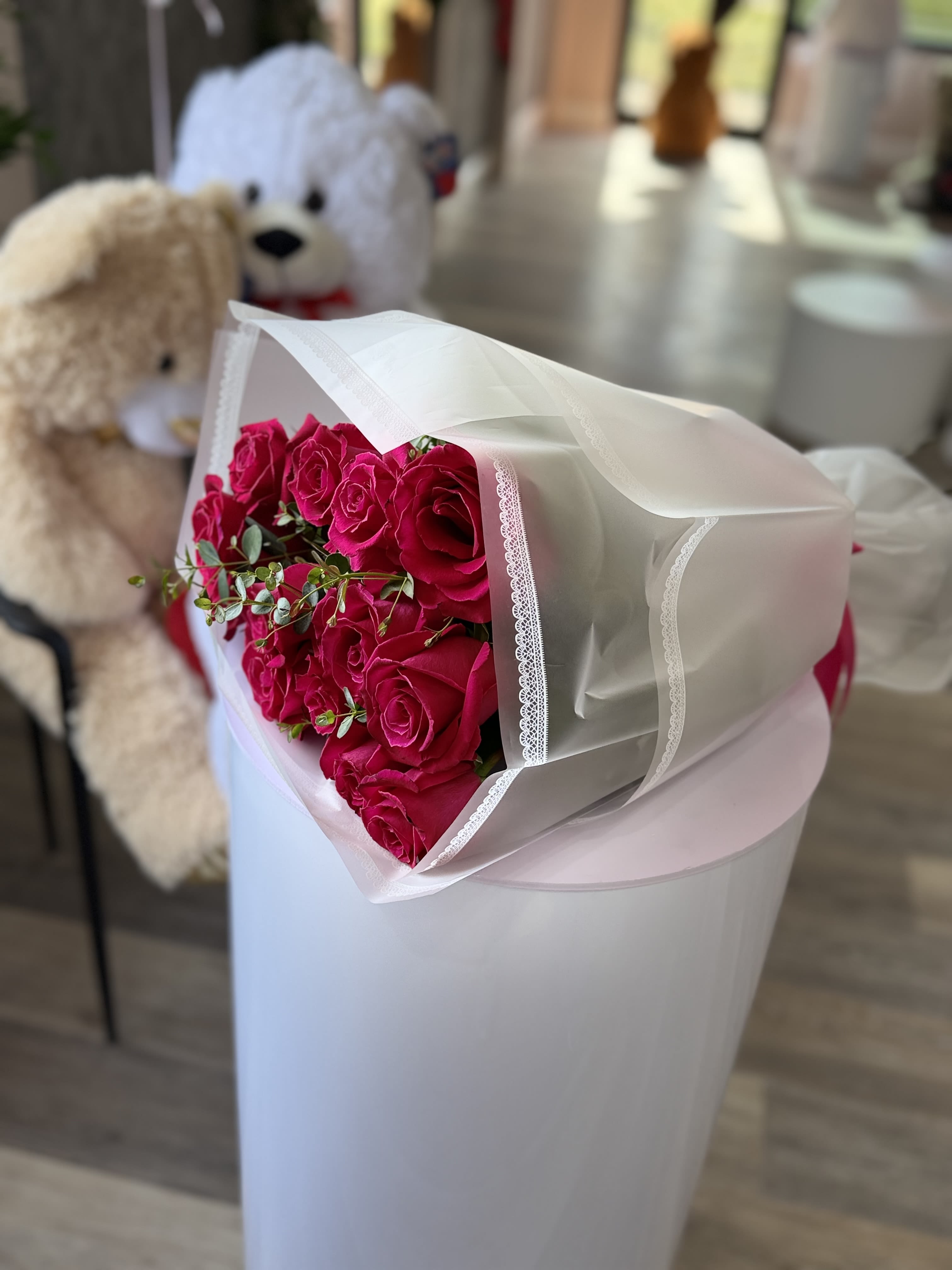 Blush Beauty - A dense cluster of vivid hot pink roses takes center stage in this romantic flower arrangement, making it an ideal choice for an anniversary bouquet, Valentine's Day gift, or any heartfelt romantic gesture. The saturated pink blooms read as joyful and passionate-she'll feel truly celebrated when presented with this lovely, gift-ready bouquet.  Tightly arranged roses are offset by small sprigs of eucalyptus-like greenery that add soft texture and a fresh green contrast. The stems are wrapped in translucent white floral paper and finished with a delicate lace trim and decorative paper wrap for a polished, classic look that feels both elegant and hand-tied.  Perfect for the person you want to make feel special-whether marking a milestone, saying "I love you," or offering thanks-this arrangement arrives ready to present. Standard care: keep stems in fresh water, recut stems if desired, and display away from direct heat to prolong bloom life.