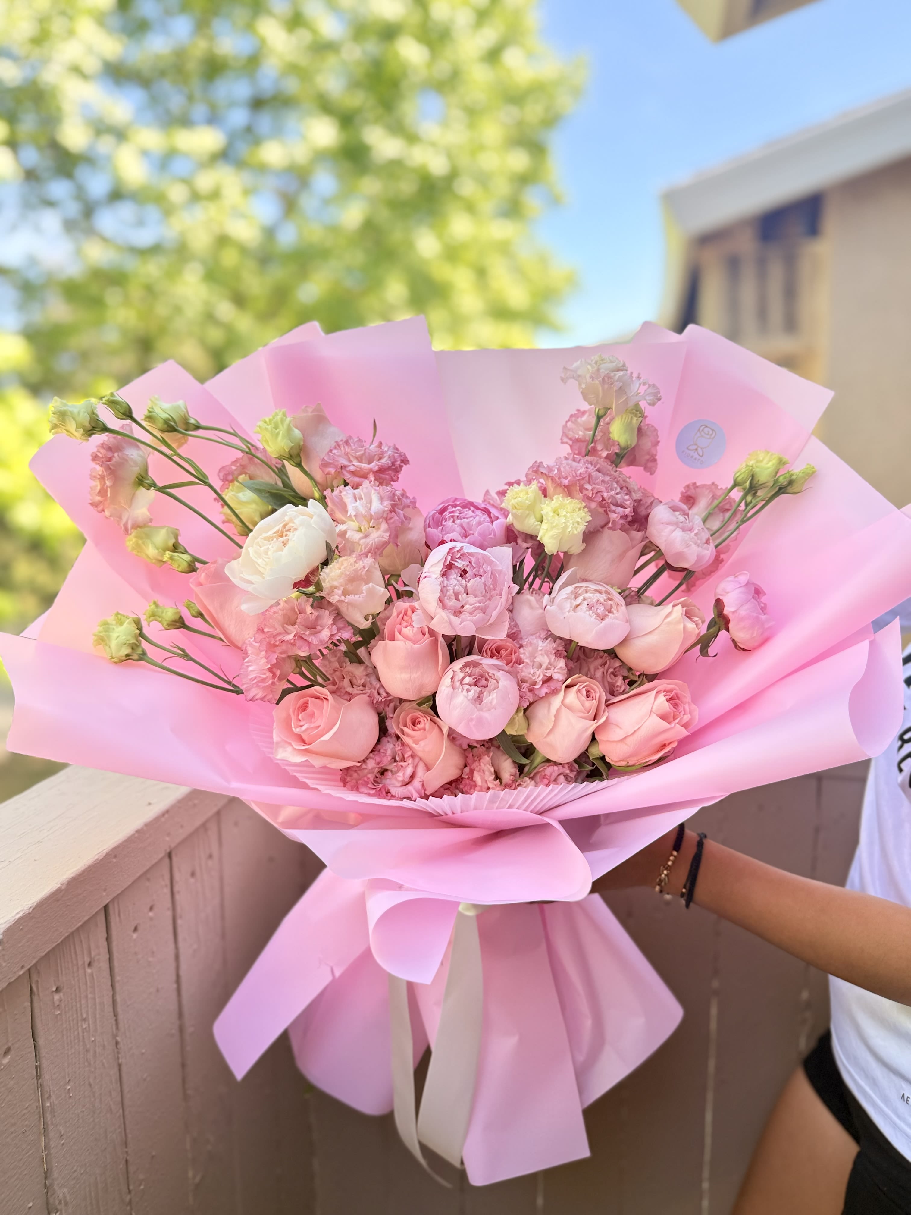 Blush Peony Garden Romance Bouquet - Fiorato Sacramento, CA. - Soft blush peonies and rounded pink roses take center stage in this romantic flower arrangement, the perfect birthday bouquet, anniversary flowers, or Mother's Day gift to make someone feel truly celebrated. Layered with pale white blooms and small ruffled pink fillers, the overall effect is lush and feminine-a spring-ready expression of affection that reads as both intimate and festive for the person you're honoring.  Hand-tied with a full, garden-style silhouette, the arrangement combines peonies, roses, carnations, and lisianthus in pink, white, and green tones for soft contrast and texture. Wrapped in oversized pastel pink paper and finished with a white ribbon, it arrives gift-ready and polished-easy to present when you want to say "you're cherished." Care: keep blooms in fresh water, trim stems and change water every other day to extend vase life.