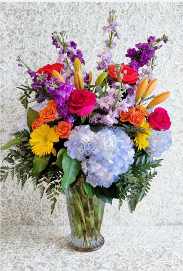 Spring Elegance  - A vibrant mix of blue hydrangeas, roses, lilies, soft lavender stock blooms, beautifully arranged in a clear glass vase.