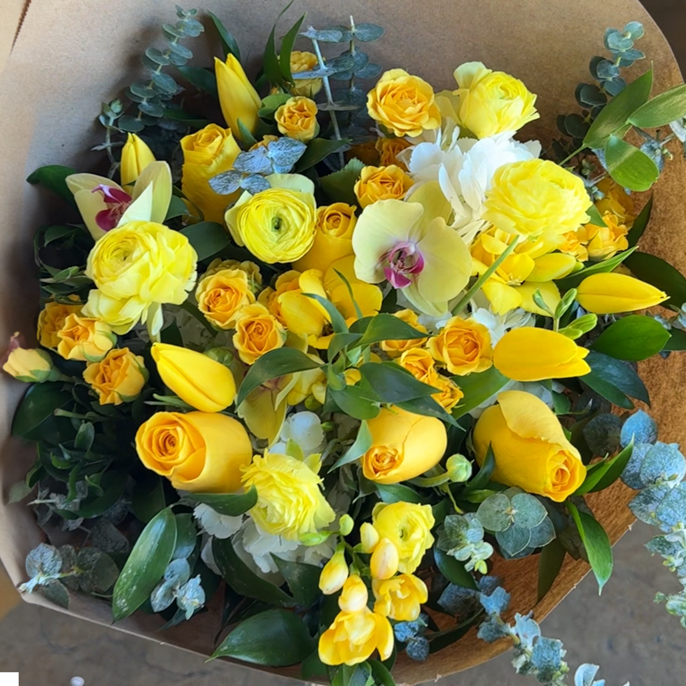 Yellow and white mixed bouquet with orchids and tulips wrapped in brown paper