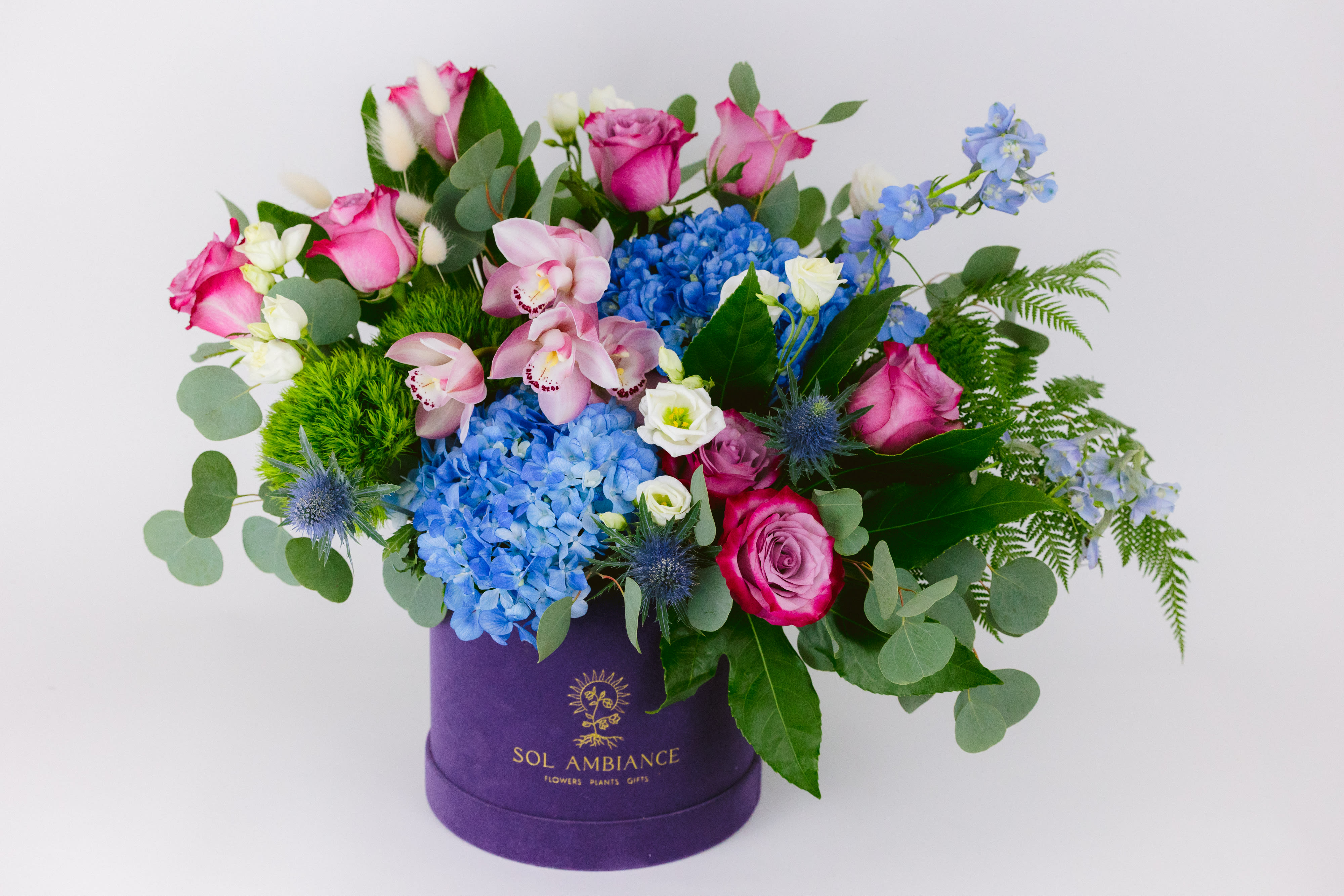 Mixed bouquet in a purple hat box with pink, blue, and white flowers