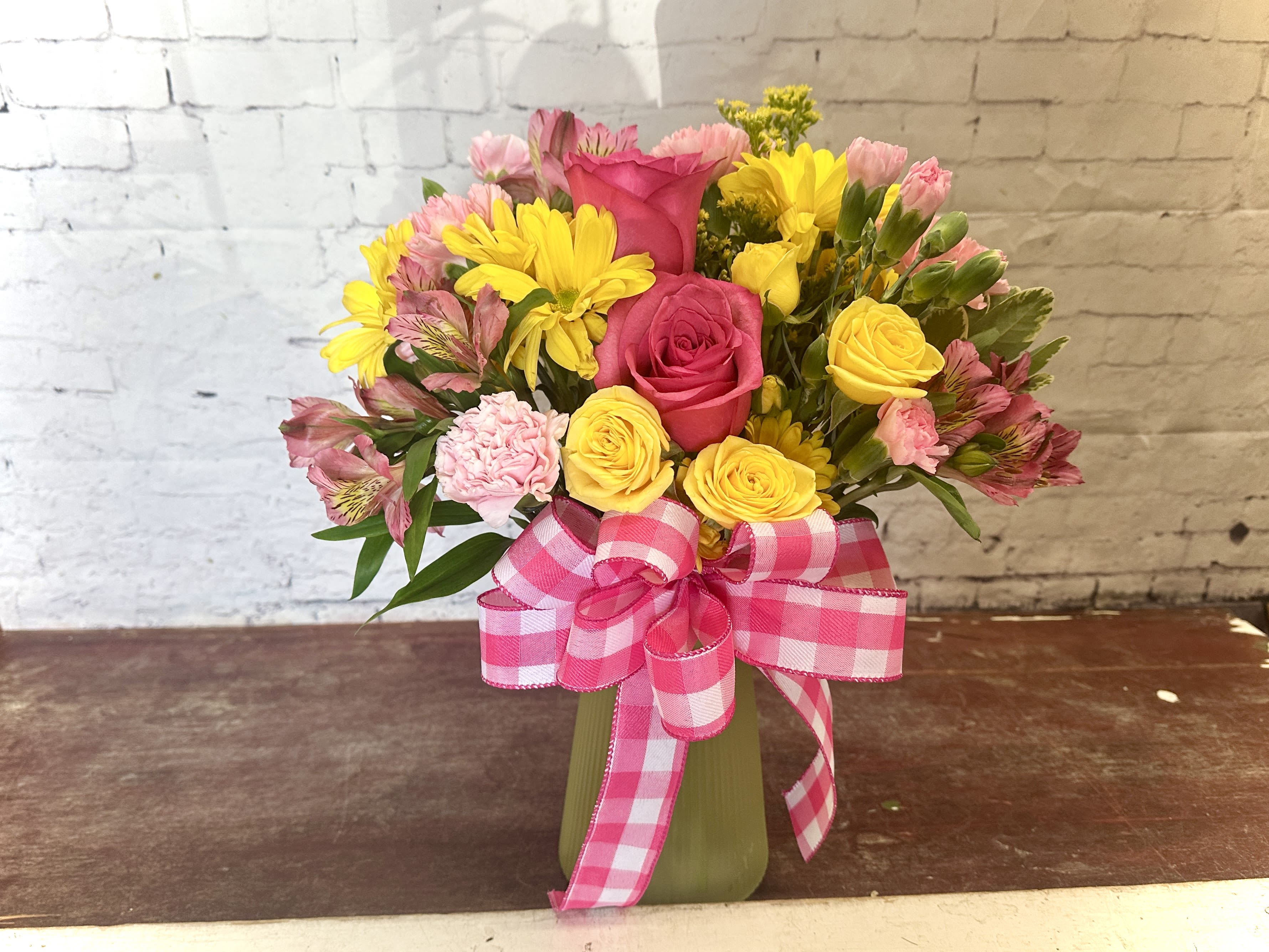 Starburst  - Mix of pink and yellow roses, carnations, alstroemeria and daisies in a yellow vase with pink ribbon.