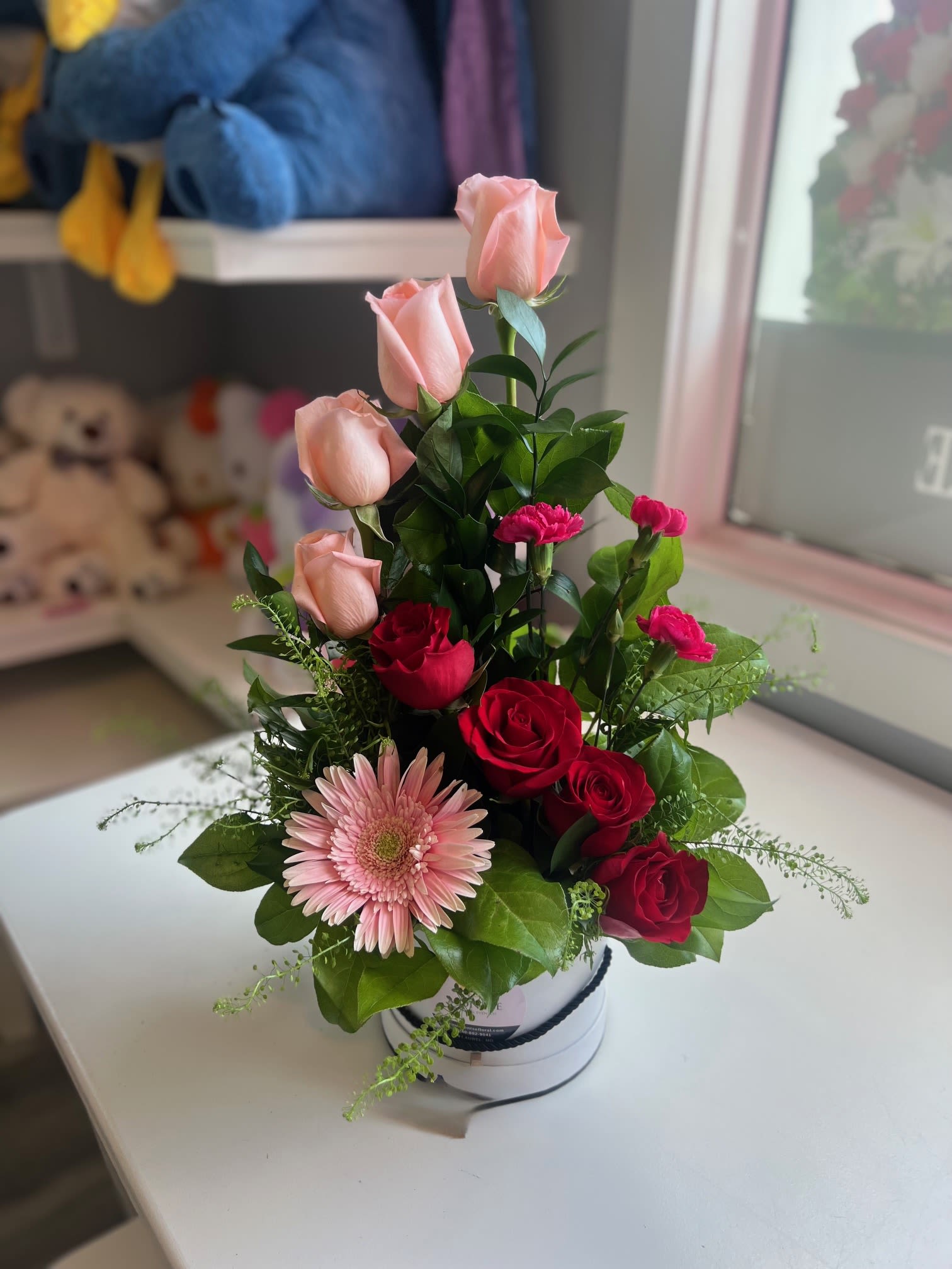 Isabella  - Compact white hat box of pink and red roses, gerbera and carnations with glossy greens 