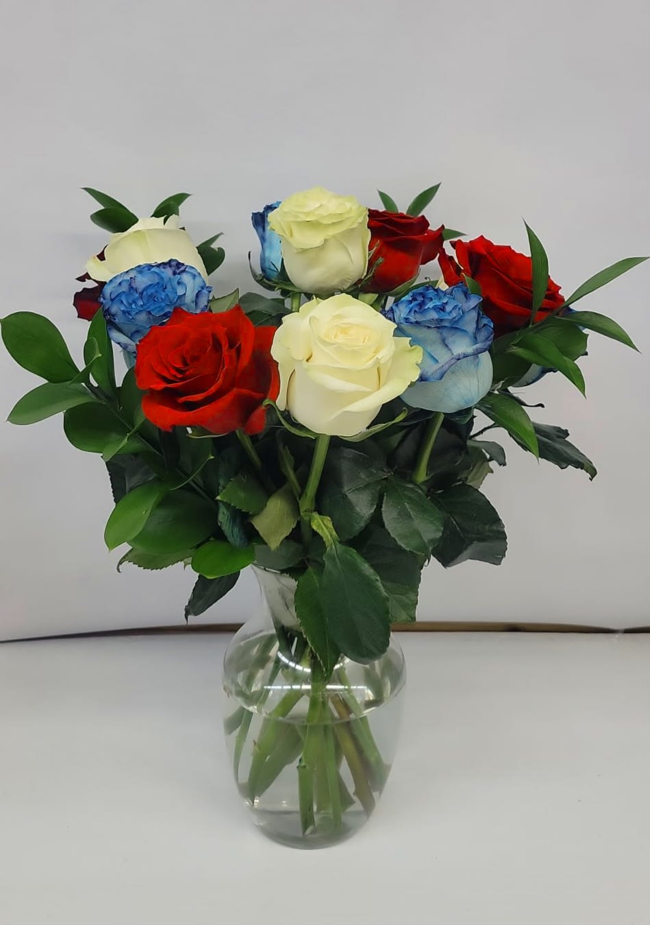 Bouquet of red, white, and blue roses in a clear glass vase
