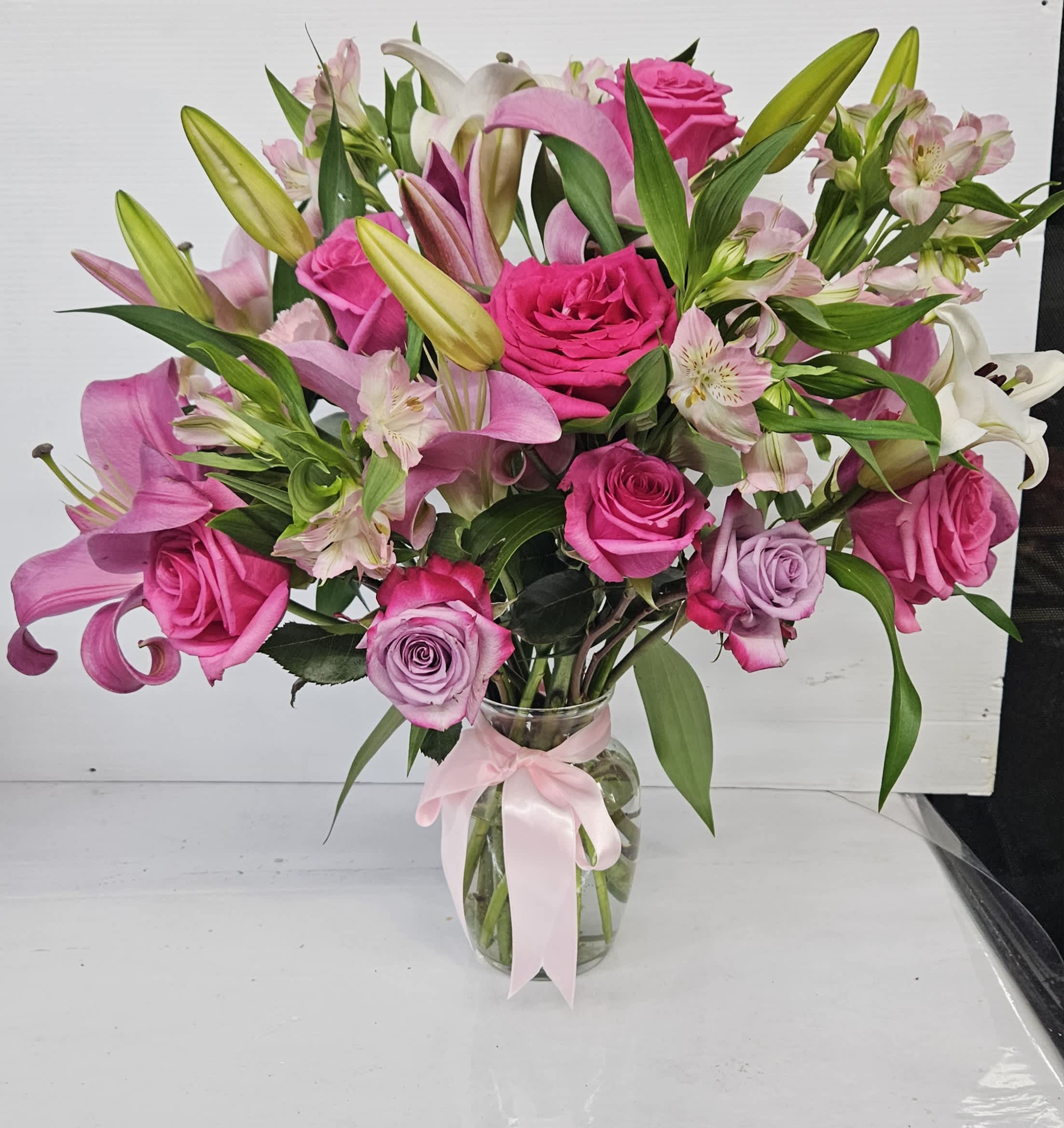 Pink roses and lilies arranged in a glass vase with a pink ribbon.