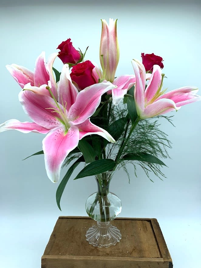 Pink lilies and red roses arranged in a clear glass vase