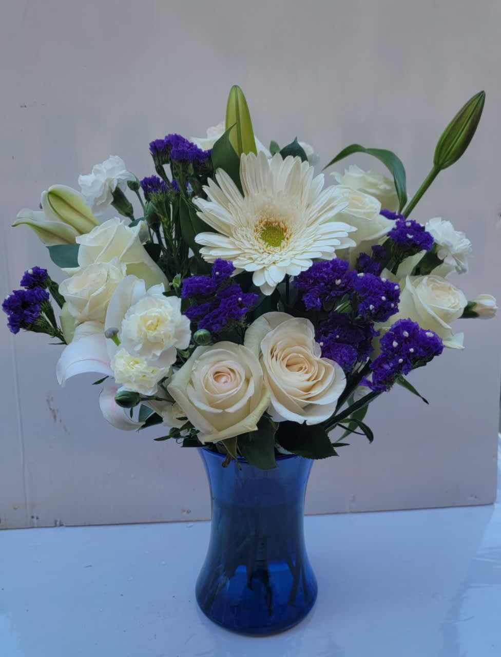 White roses and lilies with purple filler in a blue glass vase