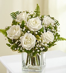 White roses arranged in a clear square vase with baby's breath