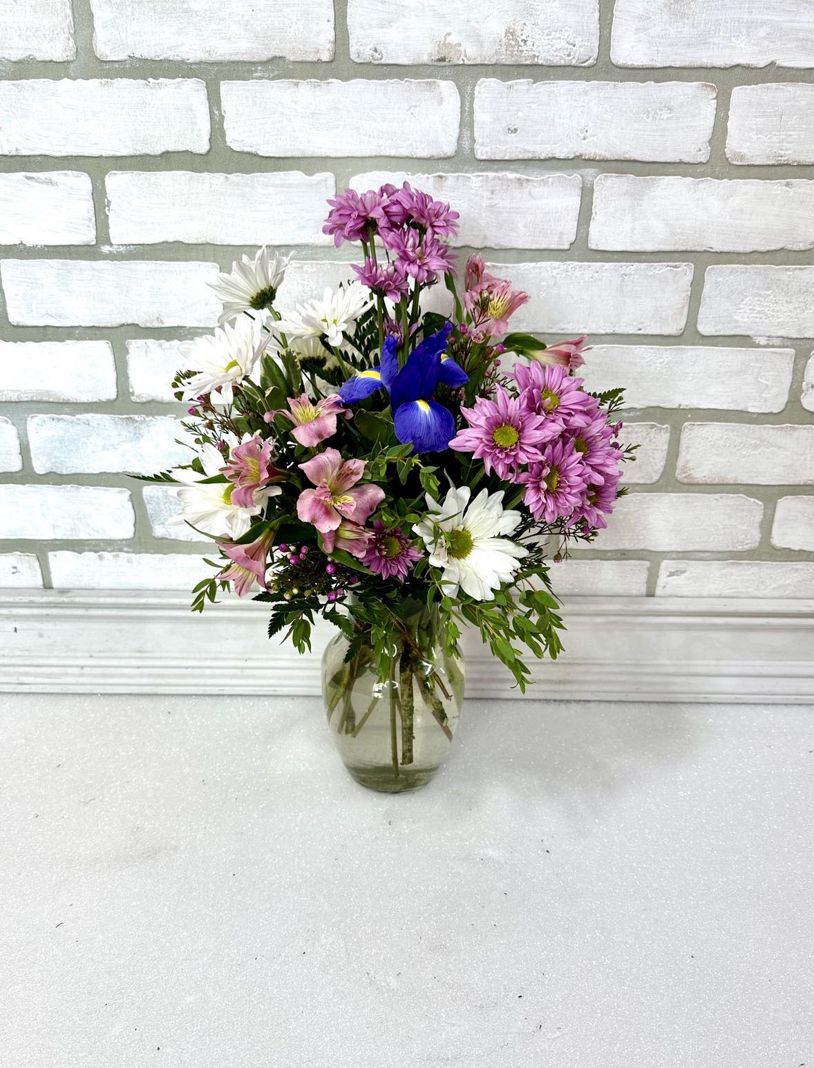 Mixed bouquet of pink, white, and blue flowers in a clear glass vase