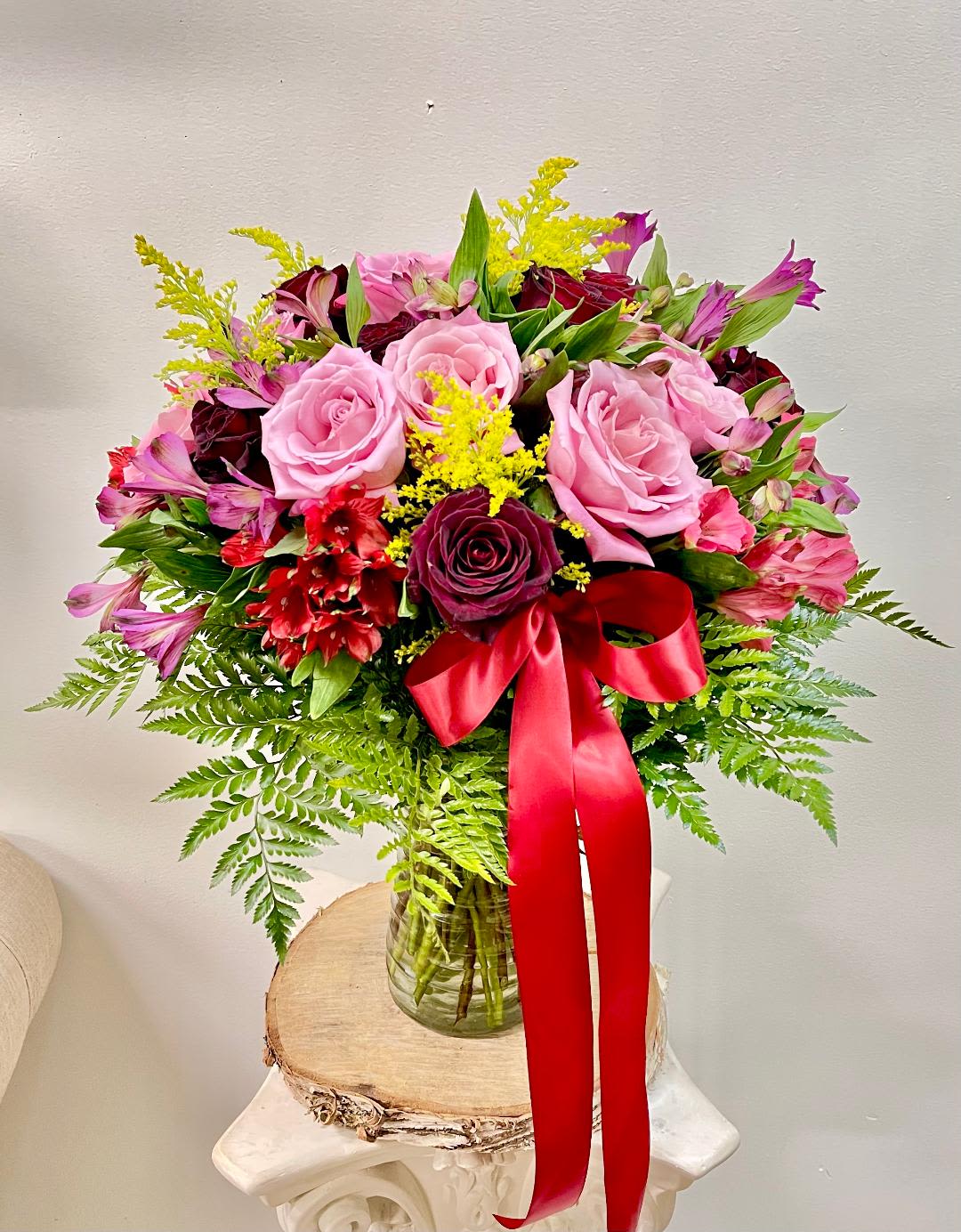 Pink and burgundy rose bouquet in a glass vase with a red ribbon