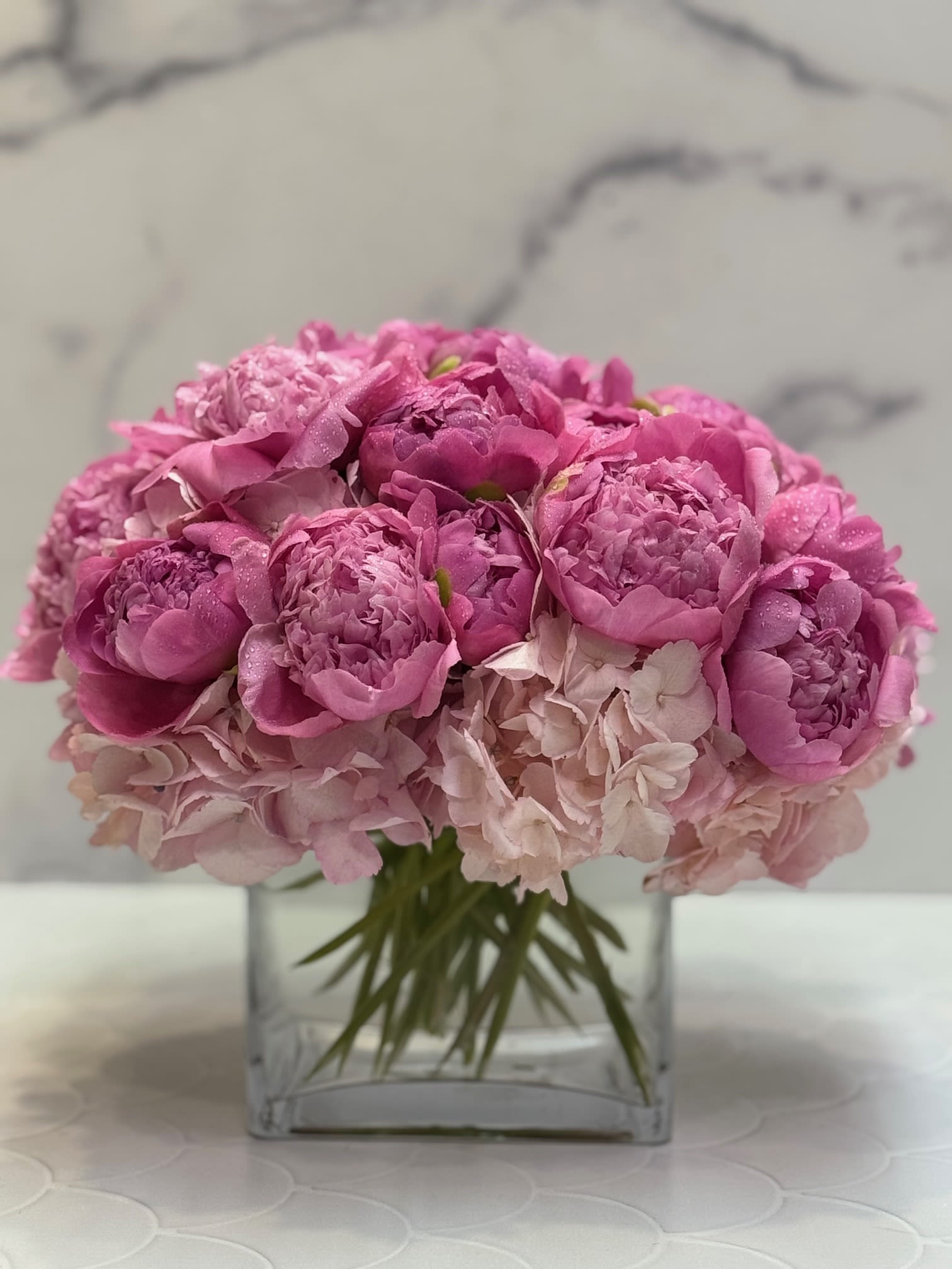 Compact arrangement of pink peonies and pale hydrangeas in a clear glass cube vase