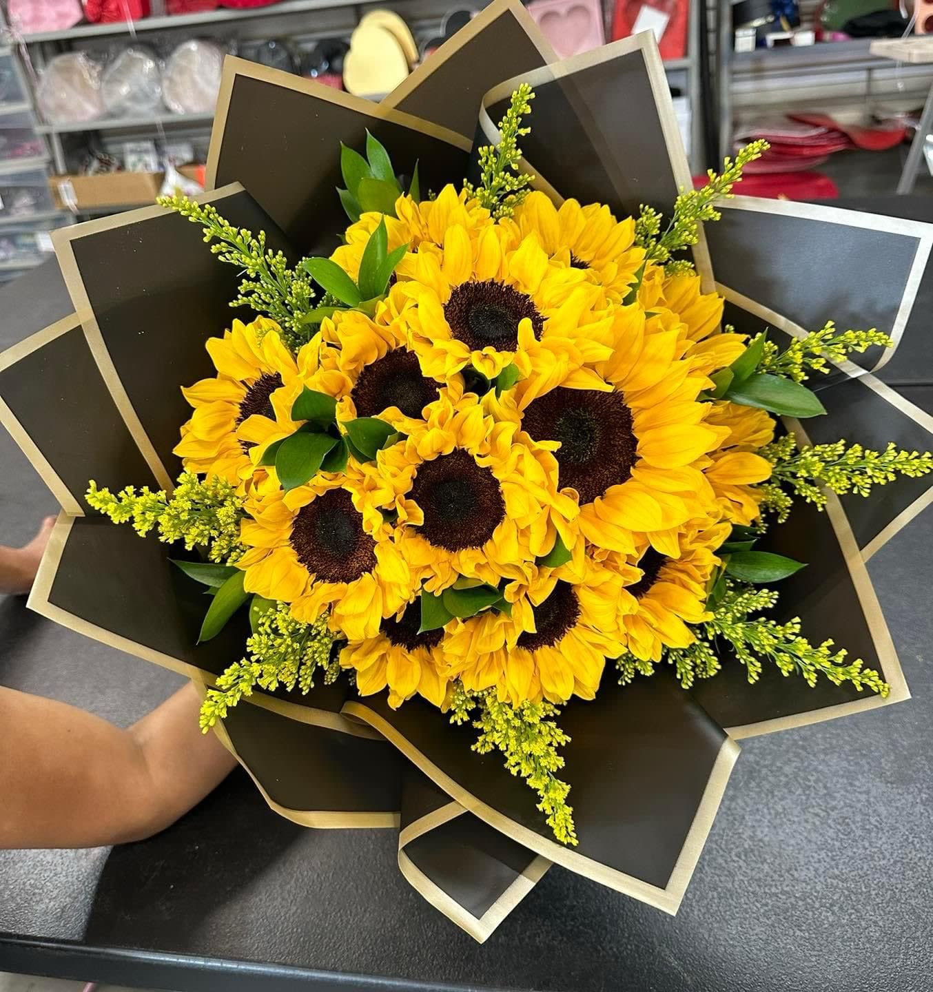 Bouquet of yellow sunflowers wrapped in black paper with gold trim