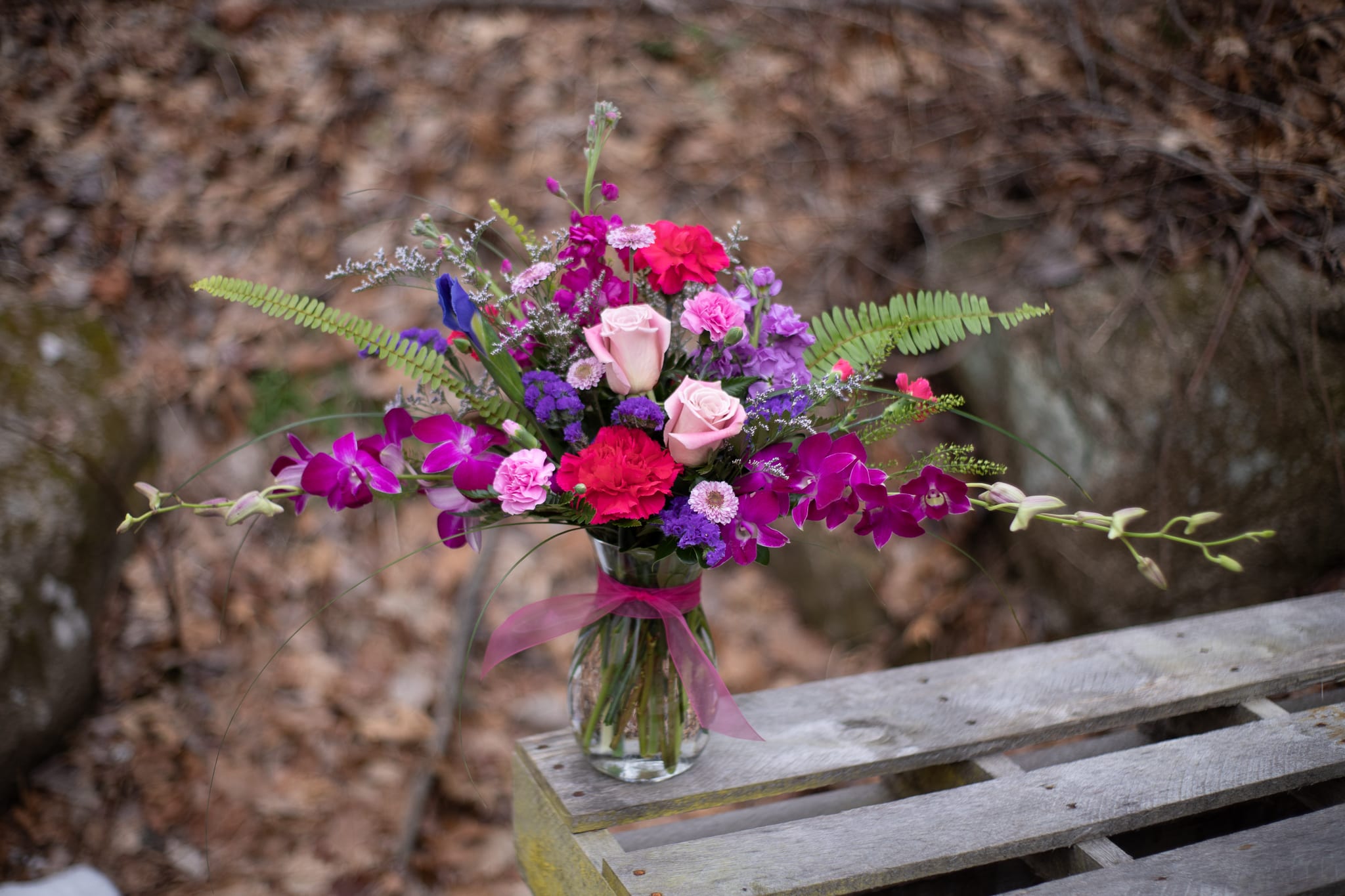 Mixed pink, purple, and red bouquet in a glass vase with a ribbon