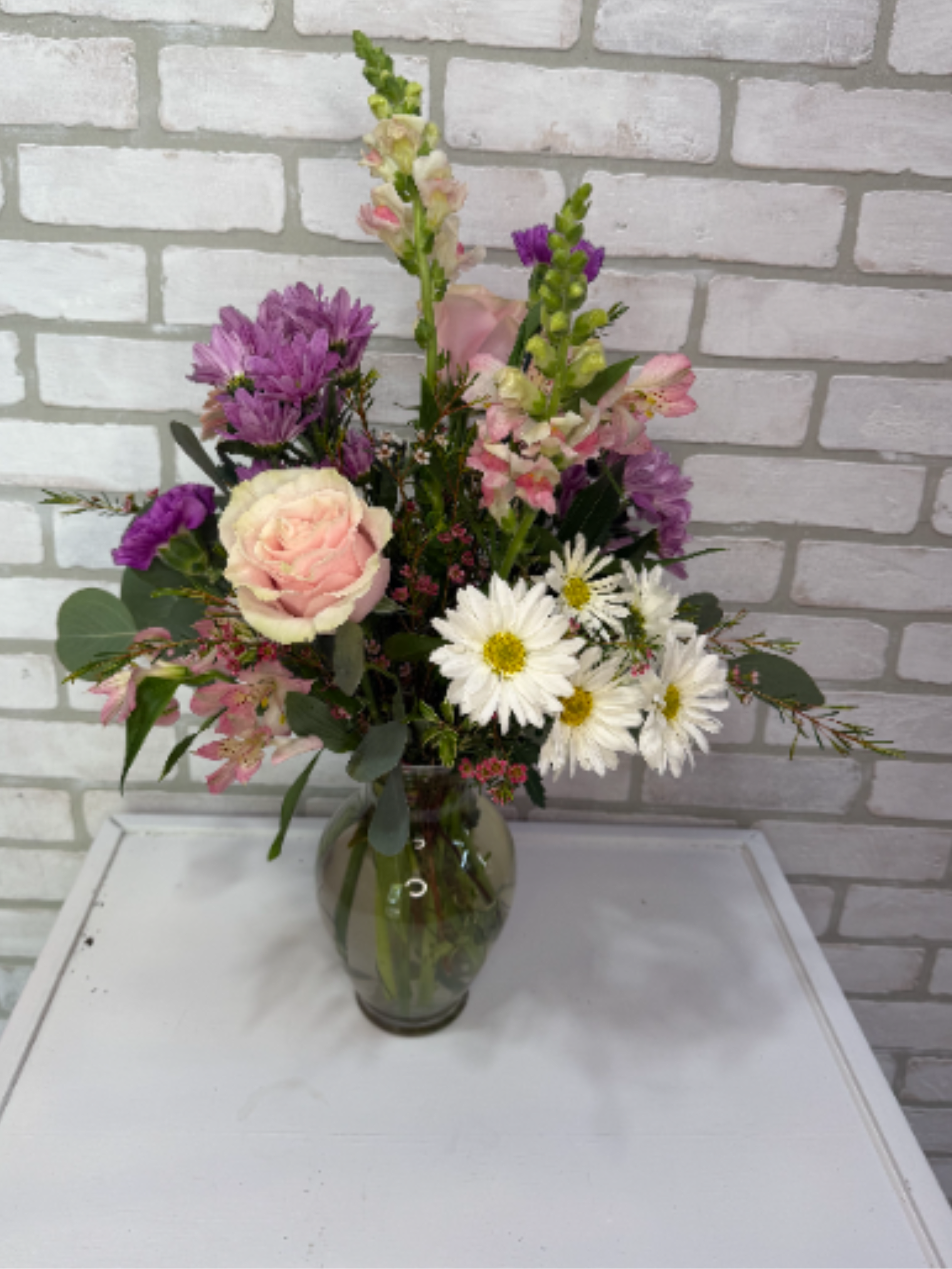 Blush of Spring - A clear vase arranged with roses, snapdragons, carnations, alstroemeria lilies, daisies, and gerbera daisies.
