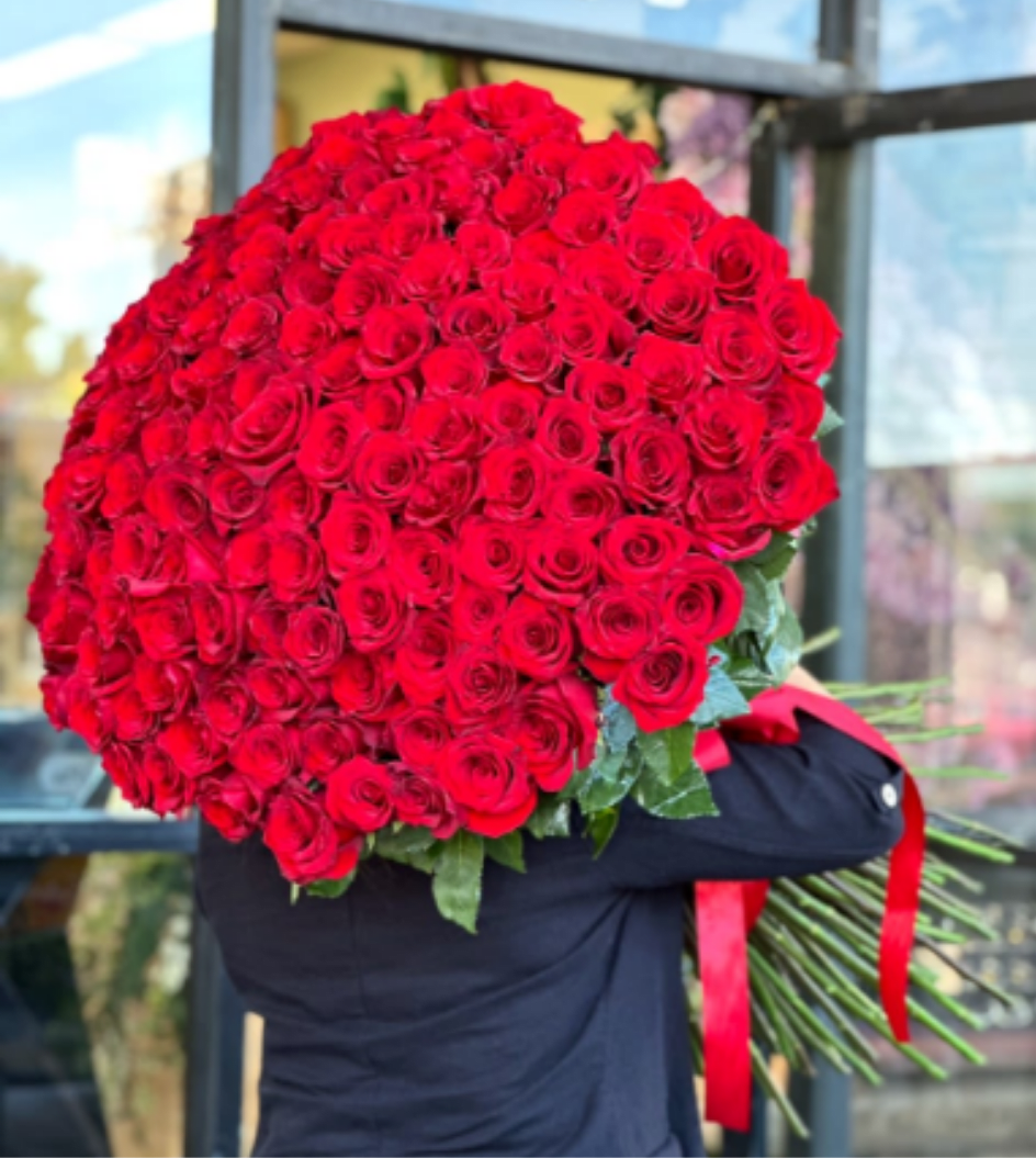 Large bouquet of red roses wrapped in dark paper with a red ribbon
