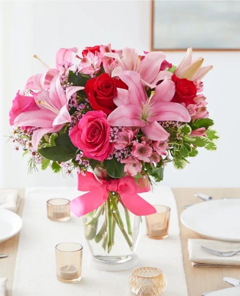 Pedals in Pink - This elegant arrangement features stunning pink oriental lilies and hot pink roses accented with delicate purple filler flowers and lush greenery perfectly finished with a signature pink satin bow in a clear vase 