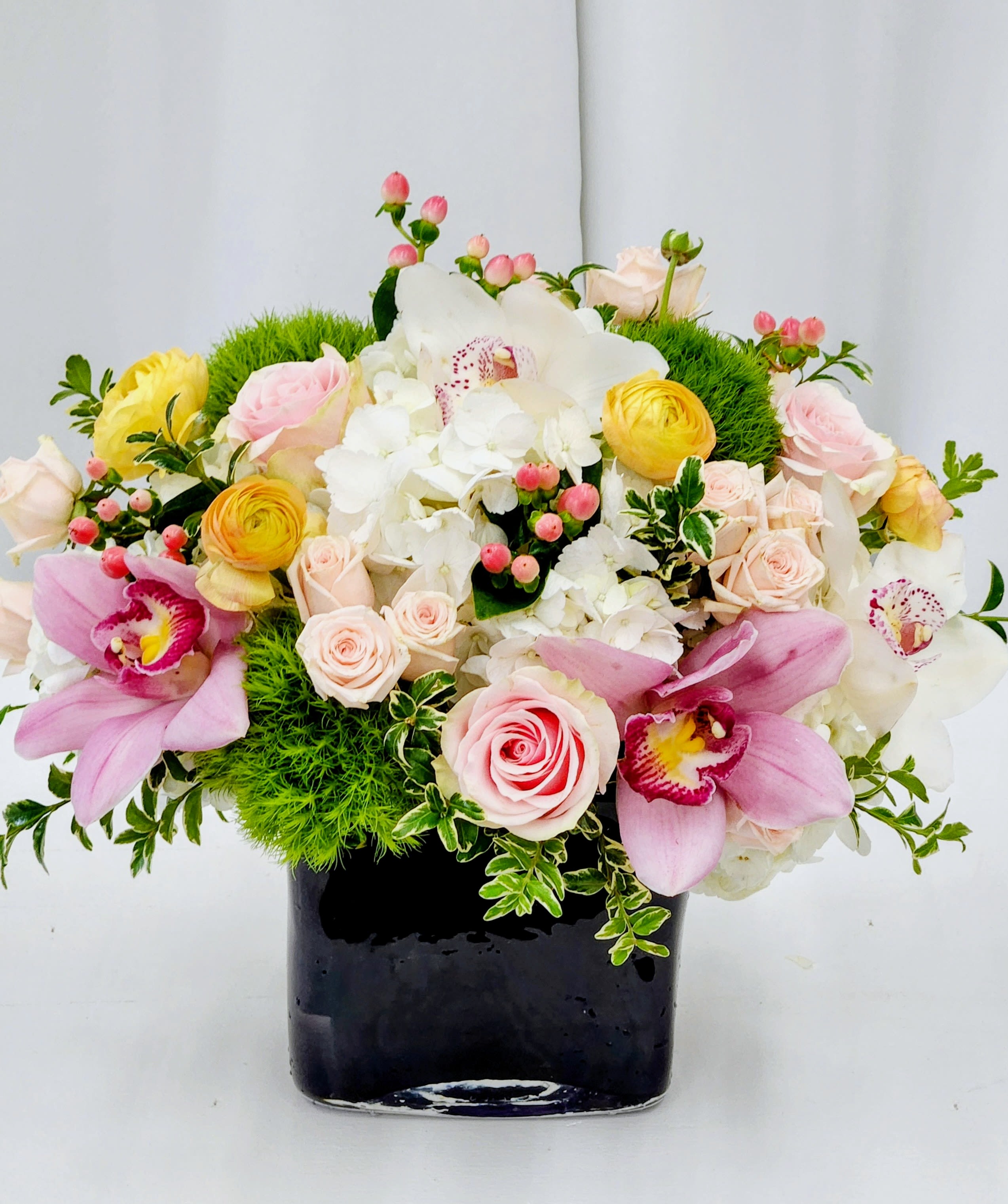 Glamming in Long Beach - Soft blush and creamy white roses mingle with pale pink orchids to create a romantic bouquet perfect for an anniversary bouquet or a wedding centerpiece. The arrangement reads feminine and refined-the kind that makes the person you're thinking of feel both cherished and adored-while the glossy black glass vase adds a modern, upscale contrast that elevates the whole gift.   