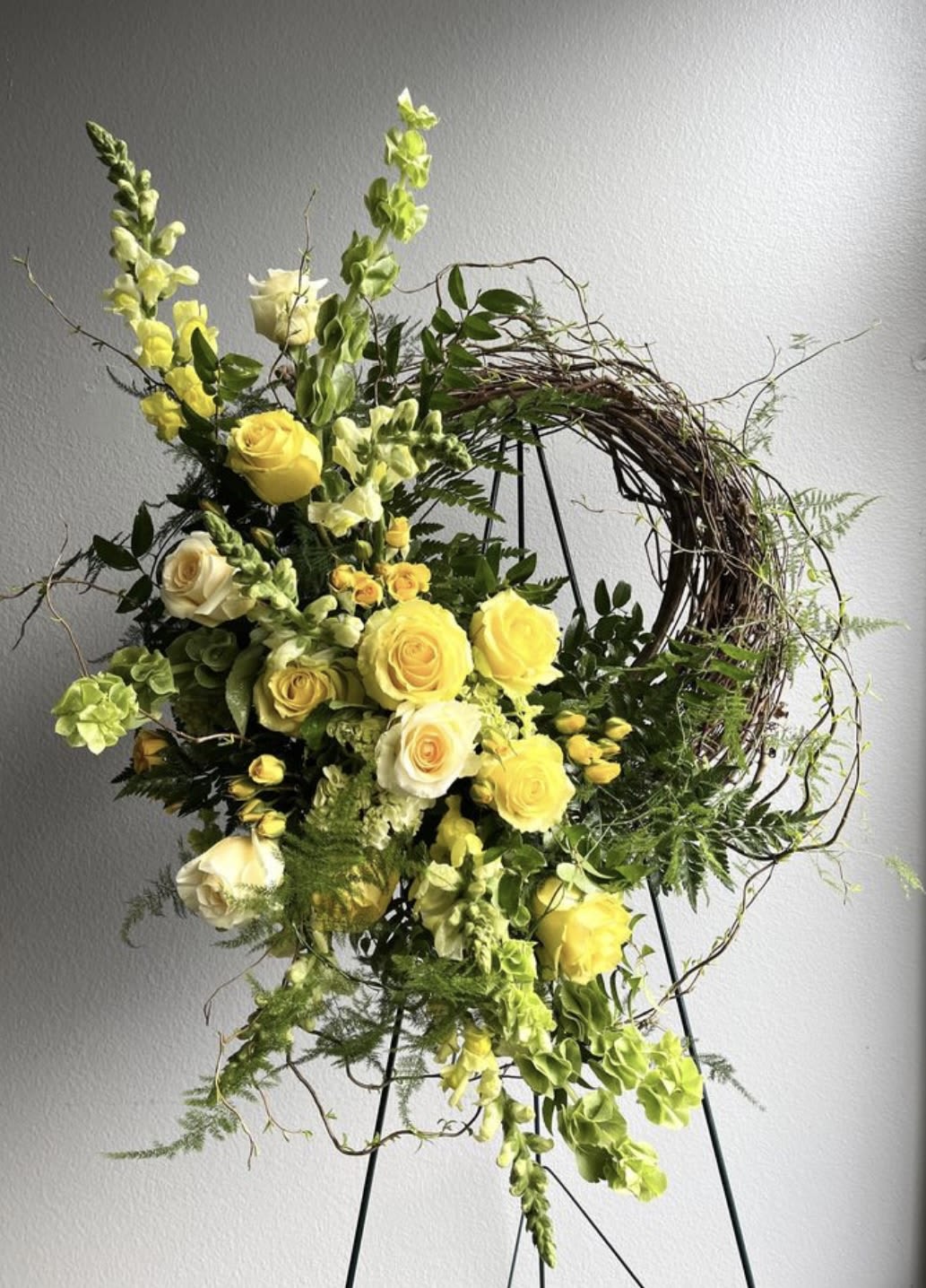 Yellow roses and snapdragons arranged on a wreath stand